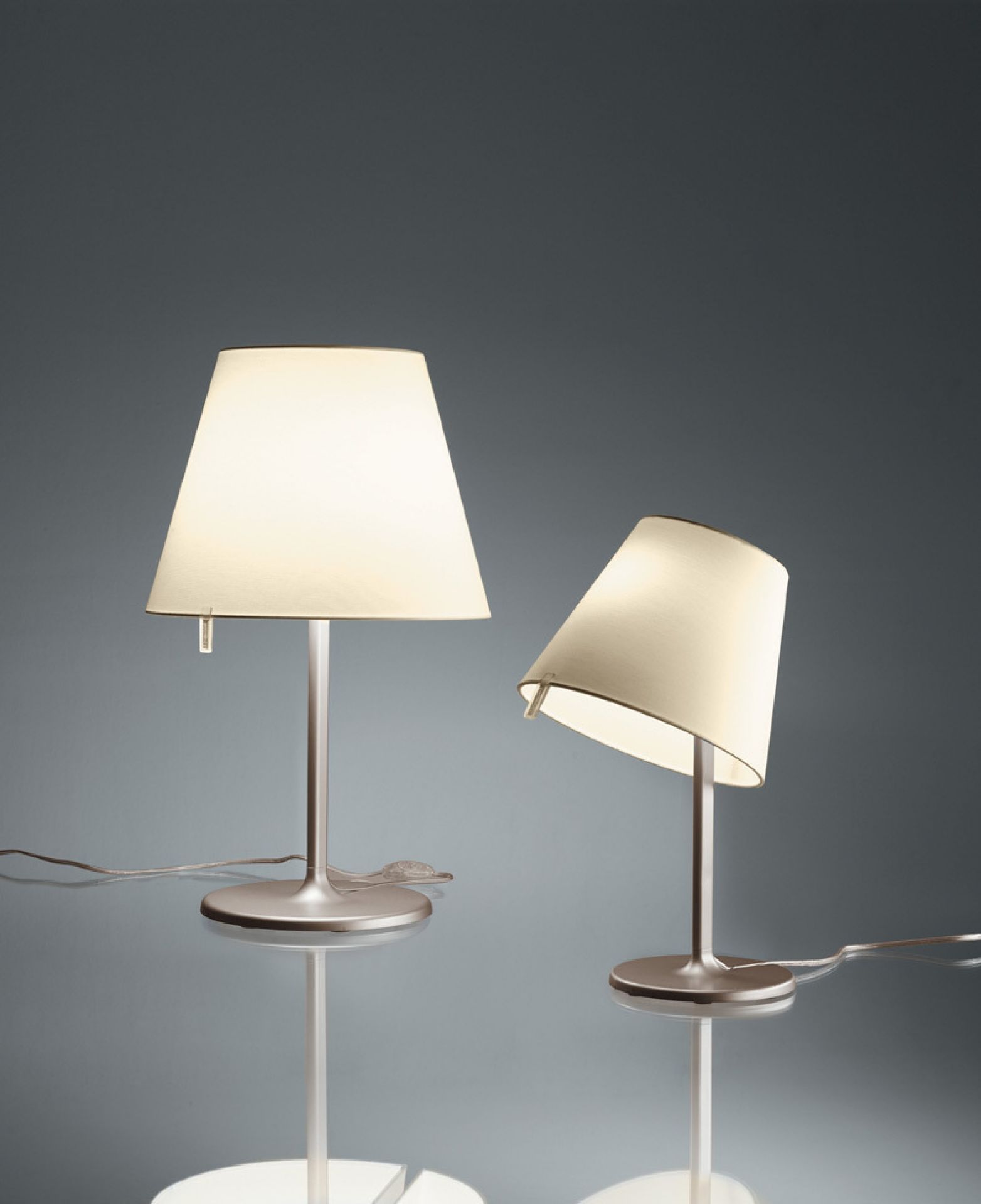 Zwei moderne Melampo Notte Tischleuchten von Artemide mit verstellbarem Schirm und sanftem Licht.
