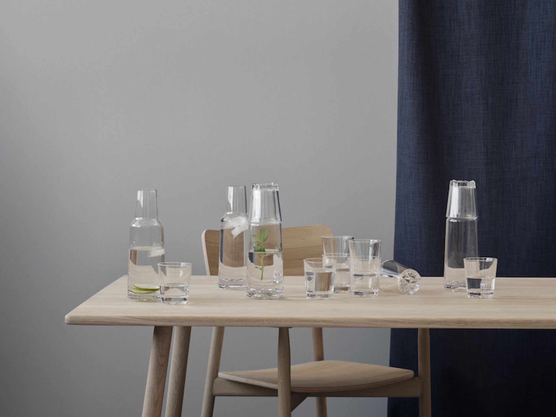 Stelton Glacier Trinkgläser: Sechs Gläser und drei Karaffen auf einem Holztisch, gefüllt mit Wasser.