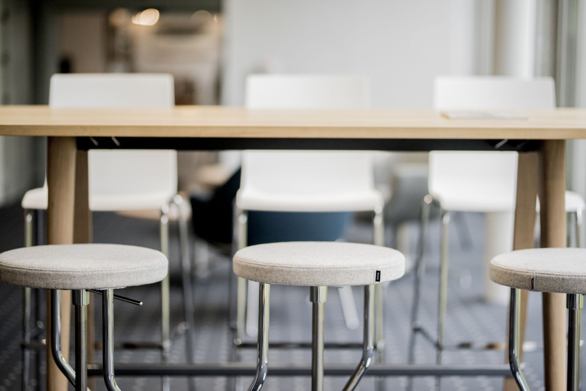 1510 Stehtisch von Thonet mit grauen Barhockern und hellen Stühlen im Hintergrund.