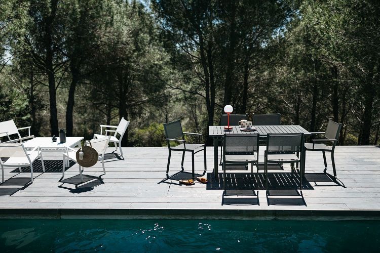 Costa Tisch von Fermob: Schwarzer Gartentisch mit Stühlen auf Holzdeck neben Pool und Bäumen.