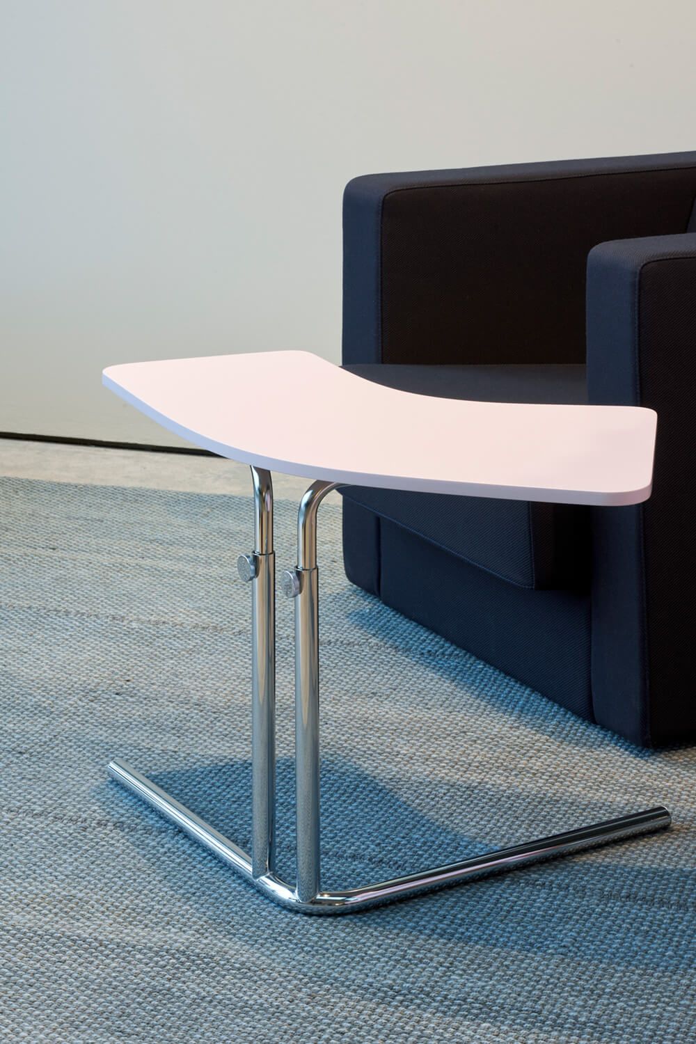 K26L Tecta Beistelltisch mit weißer Tischplatte und verchromtem Gestell neben einem Sessel.