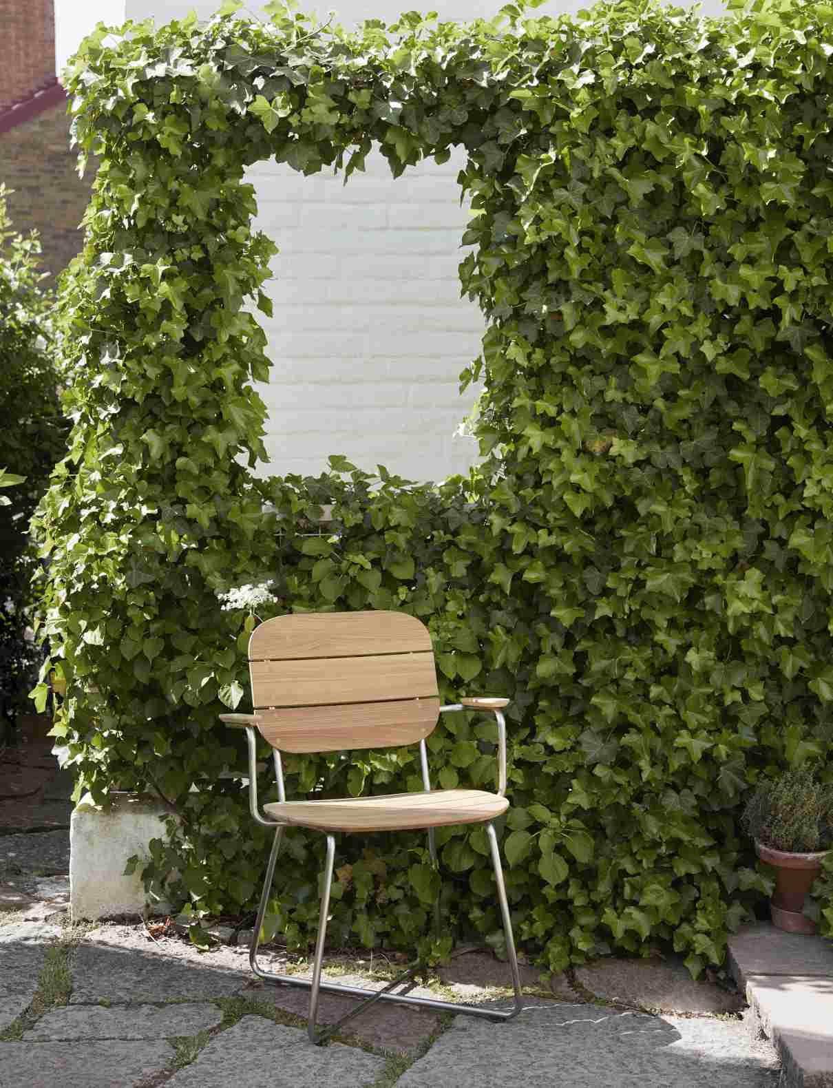 Lilium Armchair Outdoor: Armlehnenstuhl von Skagerak by Fritz Hansen vor bewachsener Wand.