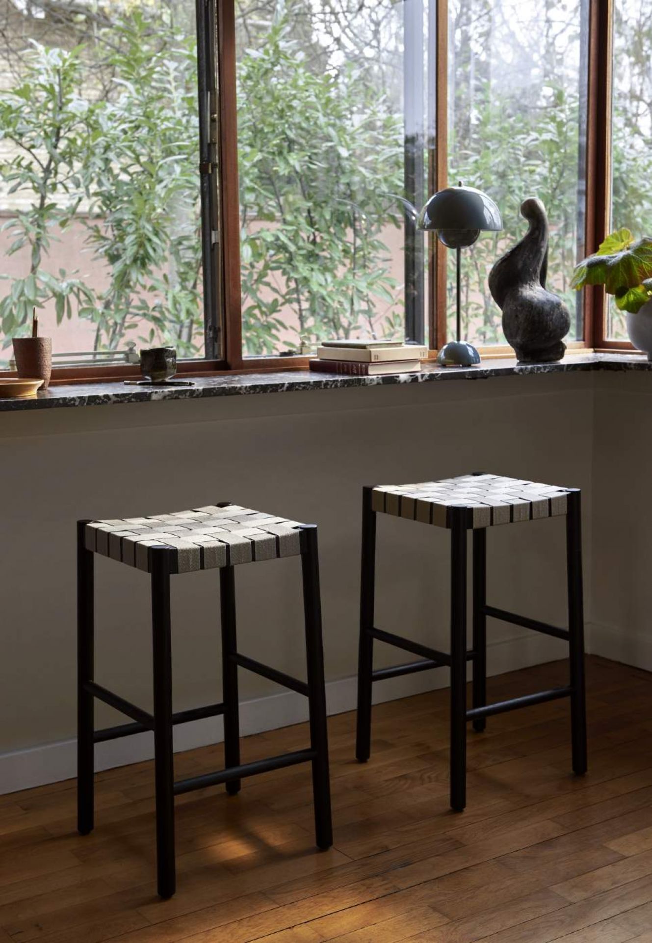 Zwei Betty TK7 Barhocker von Andtradition mit schwarzem Gestell und geflochtener Sitzfläche vor Fenster.