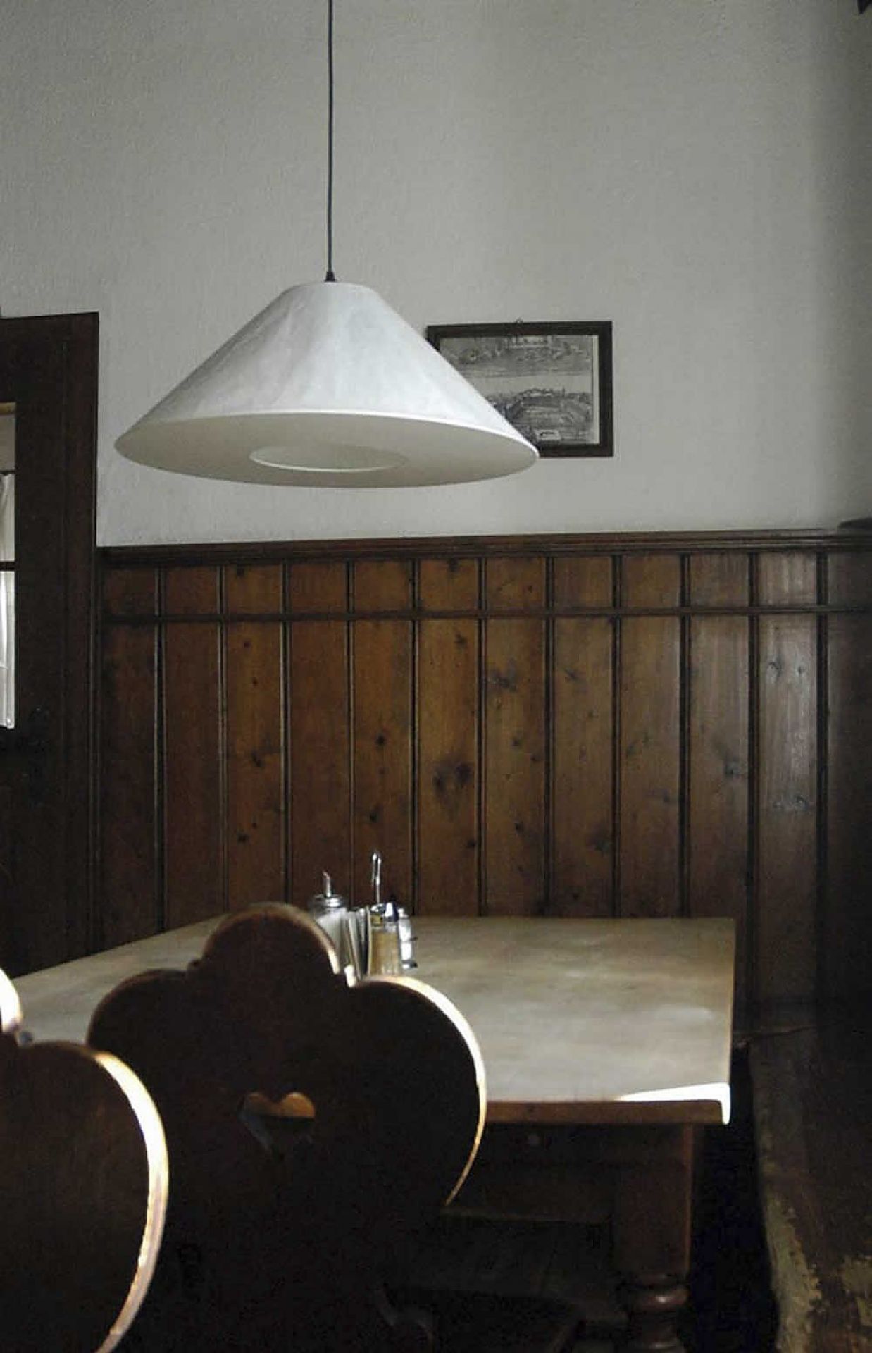 Weiße KNITTERLING Pendelleuchte von Ingo Maurer über einem Esstisch mit Holzvertäfelung.