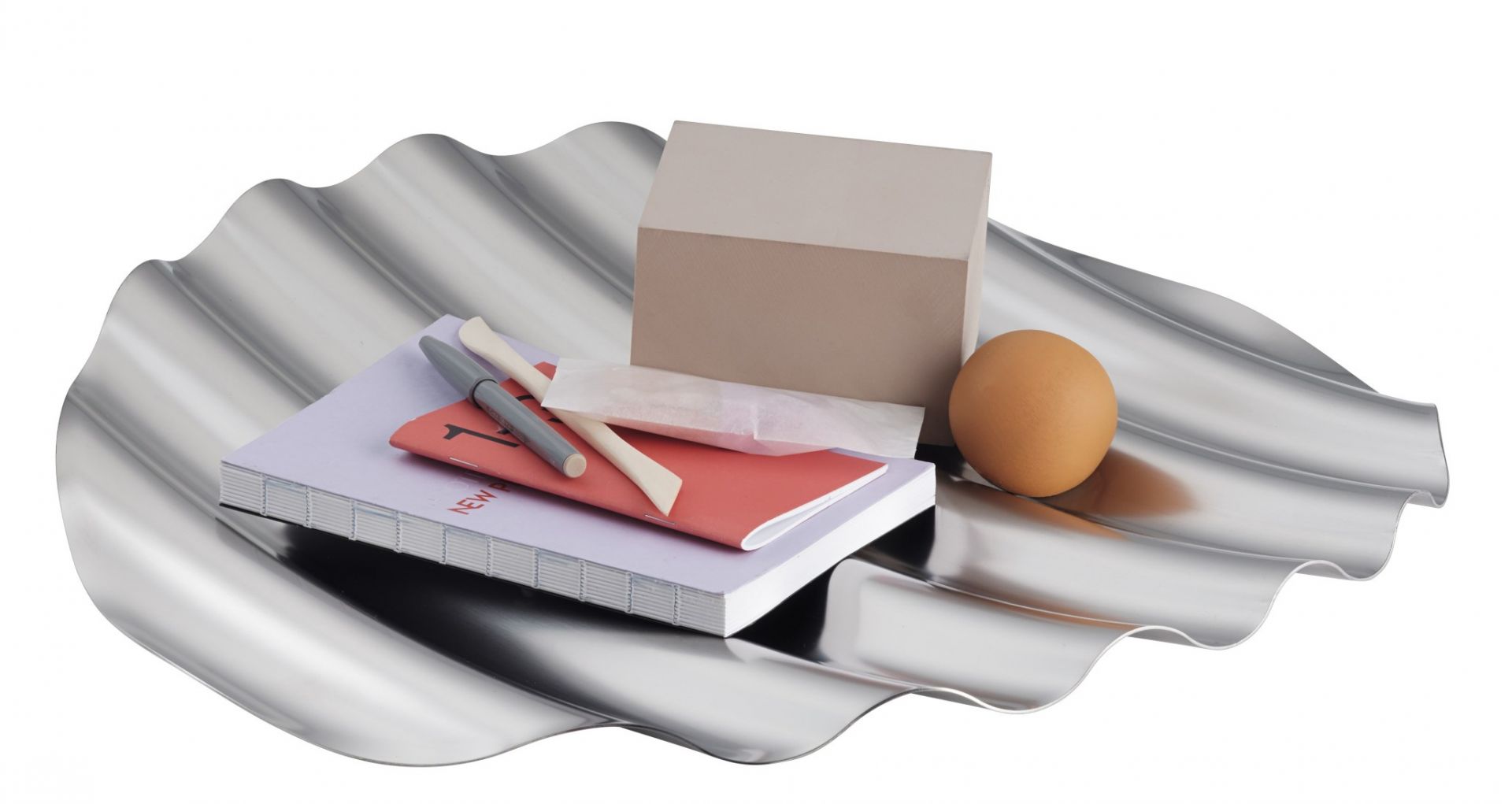Muuto Wave Tray Schale aus Edelstahl mit Notizbuch, Stiften, Ei und kleinem Paket.