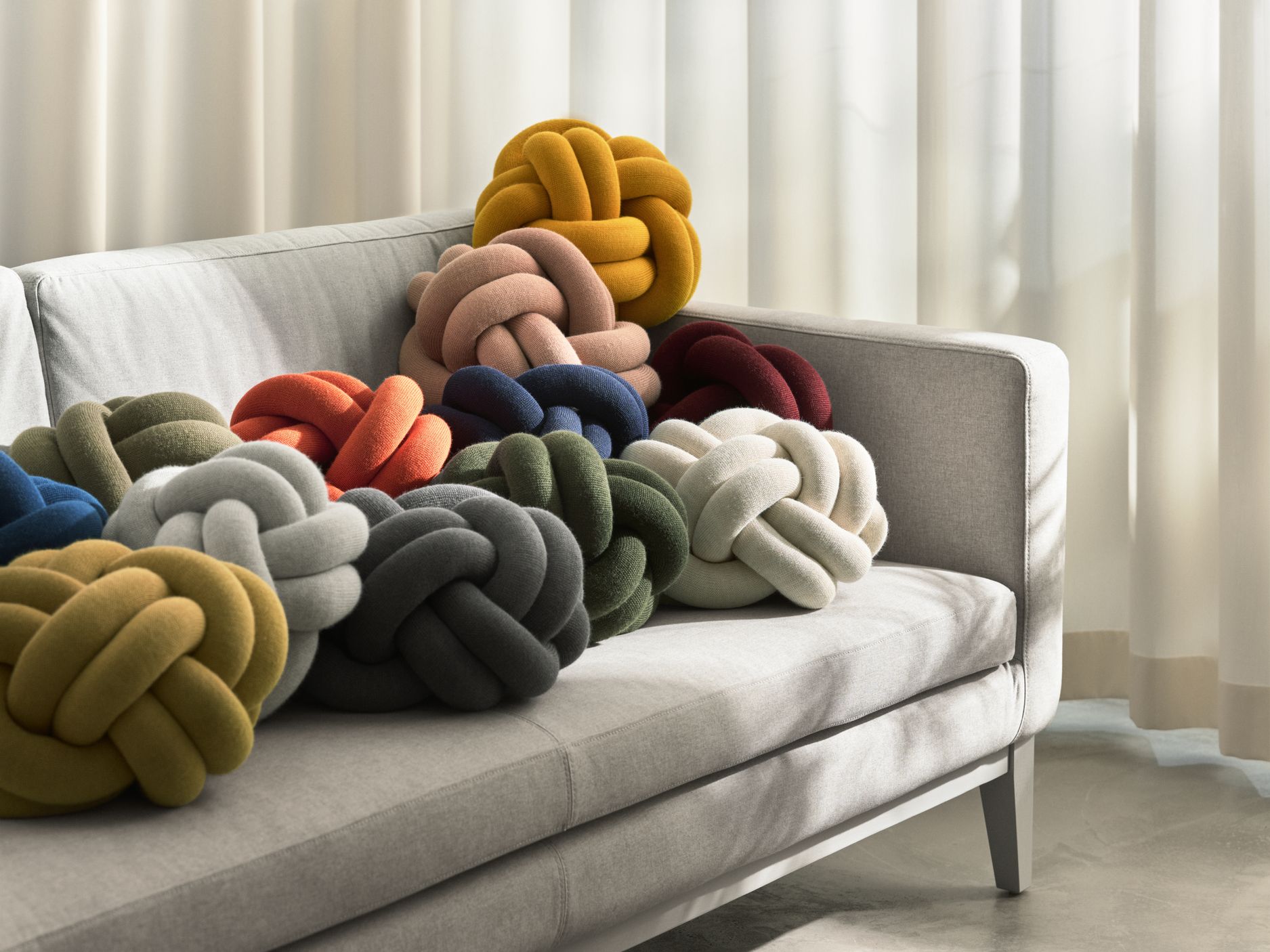 Nahaufnahme von farbenfrohen Knot Kissen von Design House Stockholm auf einem grauen Sofa. Dekorative Knoten Kissen.