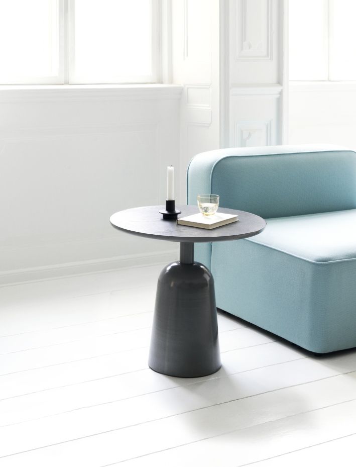 Normann Copenhagen Turn Table Tisch in Grau, mit Kerze, Buch und Glas auf weißem Holzboden.