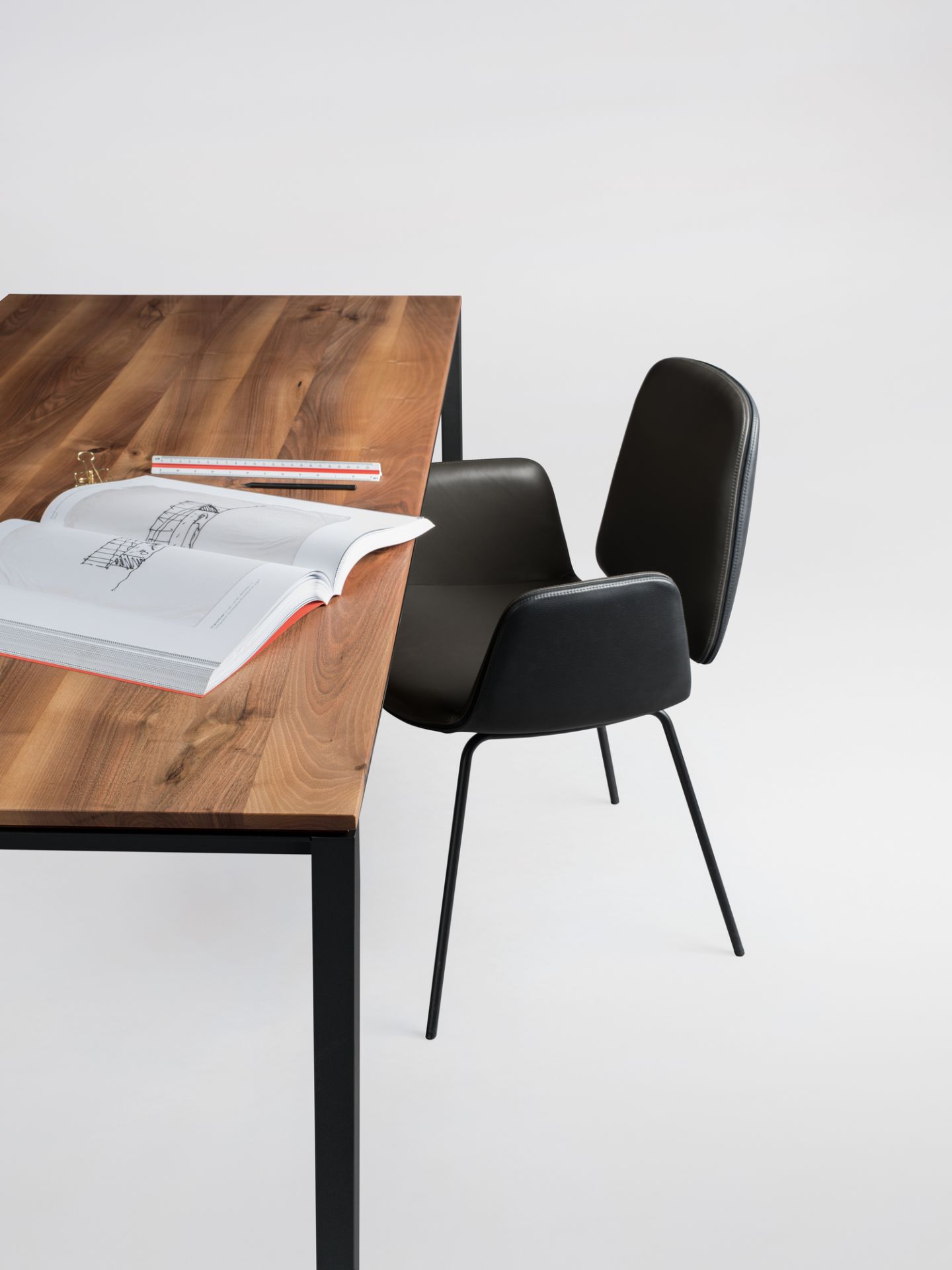 Janua S 600 Tisch mit Nussbaumplatte und schwarzem Stahlgestell, daneben ein schwarzer Stuhl.