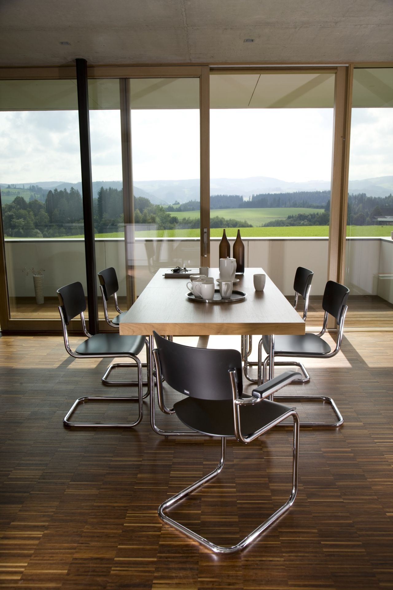 Esszimmer mit Thonet S 1071 Esstisch, ausziehbar, Holzplatte und Freischwinger Stühlen vor Panoramafenster.
