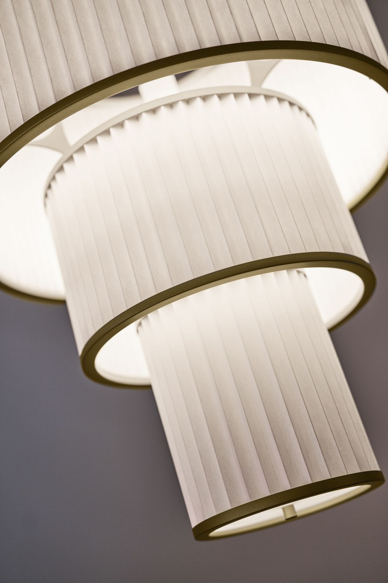 Nahaufnahme der Plivello Pendelleuchte von Le Klint mit plissiertem Lampenschirm und warmem Licht.