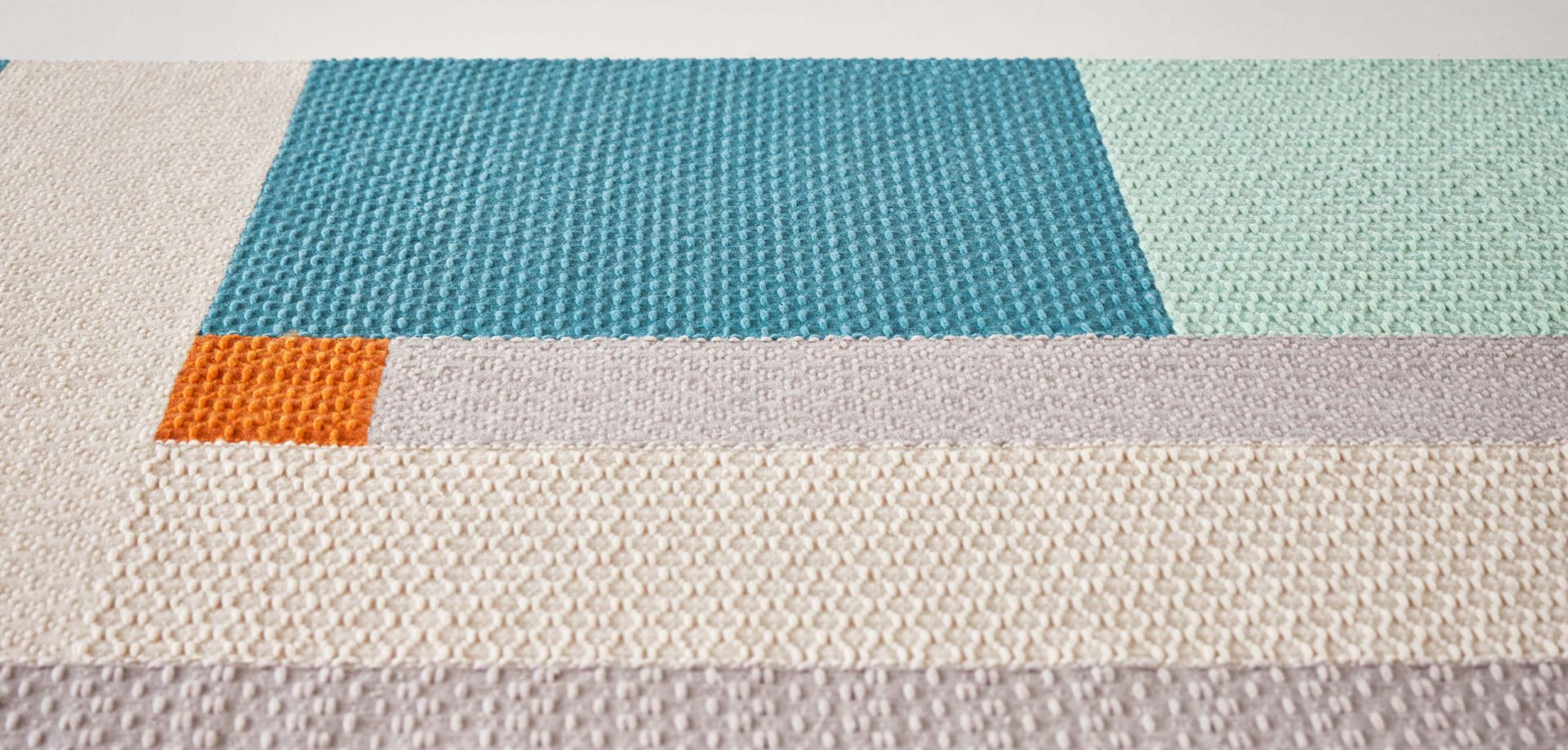 Detailaufnahme des Weave Rug Teppichs Meeting Point Gan mit geometrischem Muster in Blau, Orange, Grau und Beige.