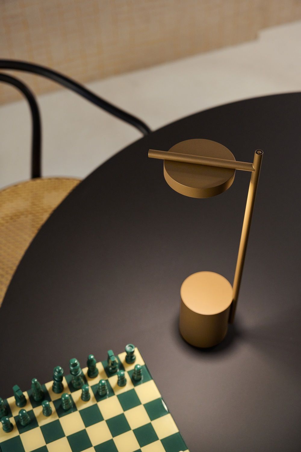 Messingfarbene Igram Tischleuchte von Grupa auf schwarzem Tisch neben Schachbrett. Akkuleuchte für stimmungsvolle Beleuchtung.
