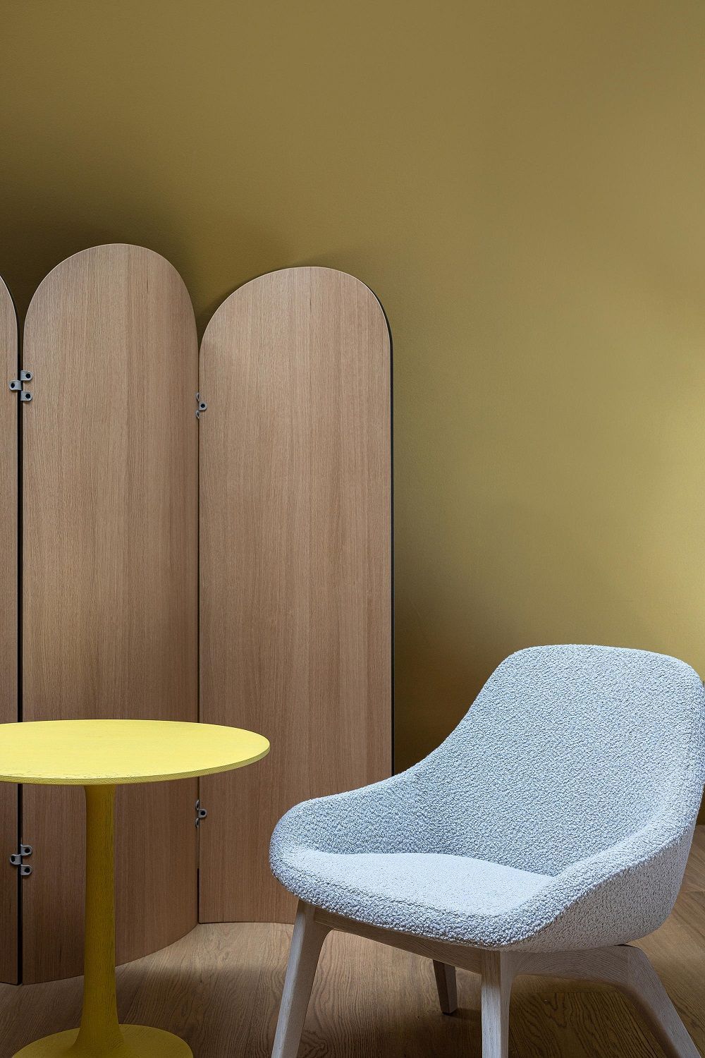 Ad Just Paravent Raumteiler aus Holz neben gelbem Tisch und blauem Sessel.