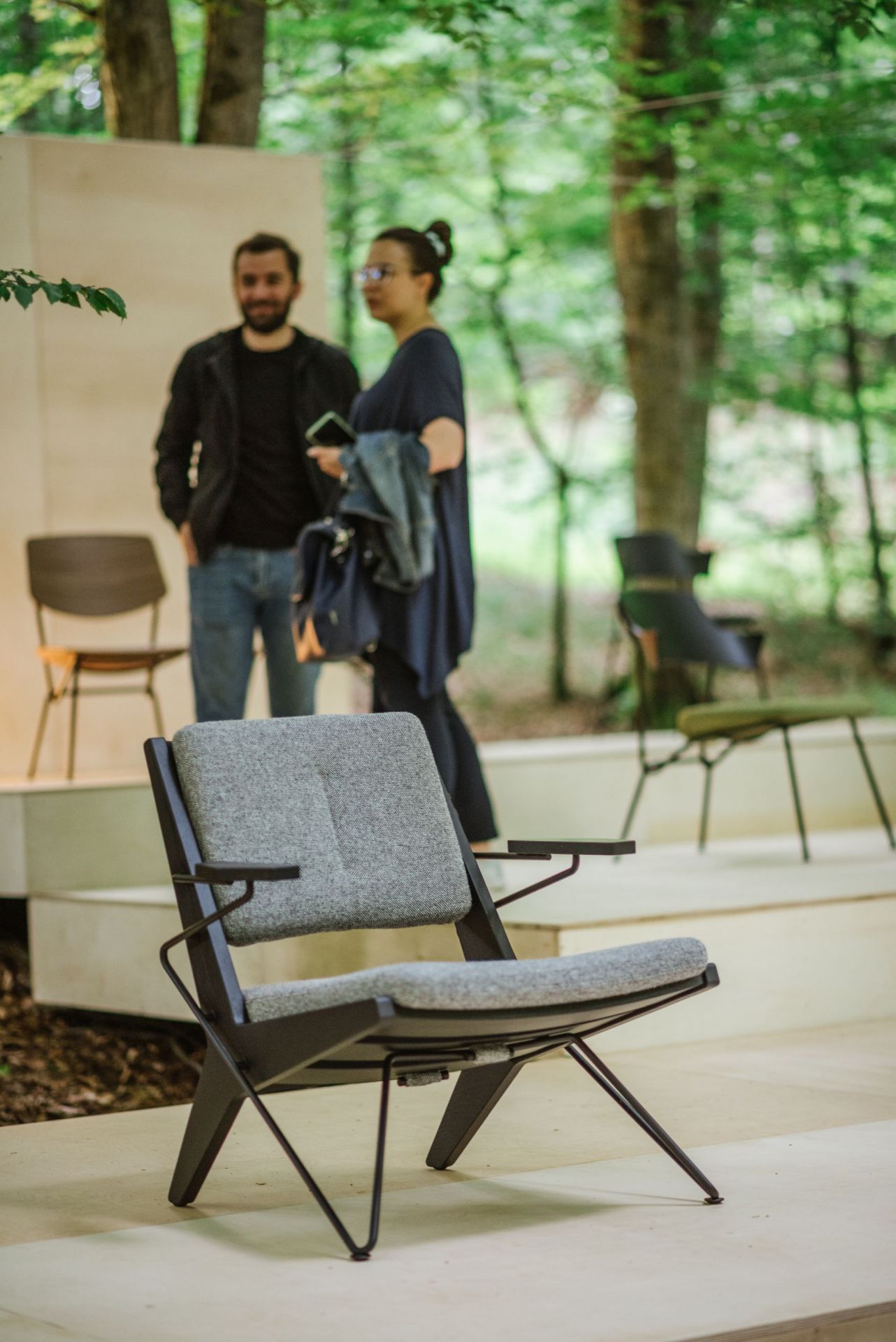 Grauer Toggle Sessel aus Holz von Prostoria mit Armlehnen und Metallbeinen vor natürlicher Kulisse.