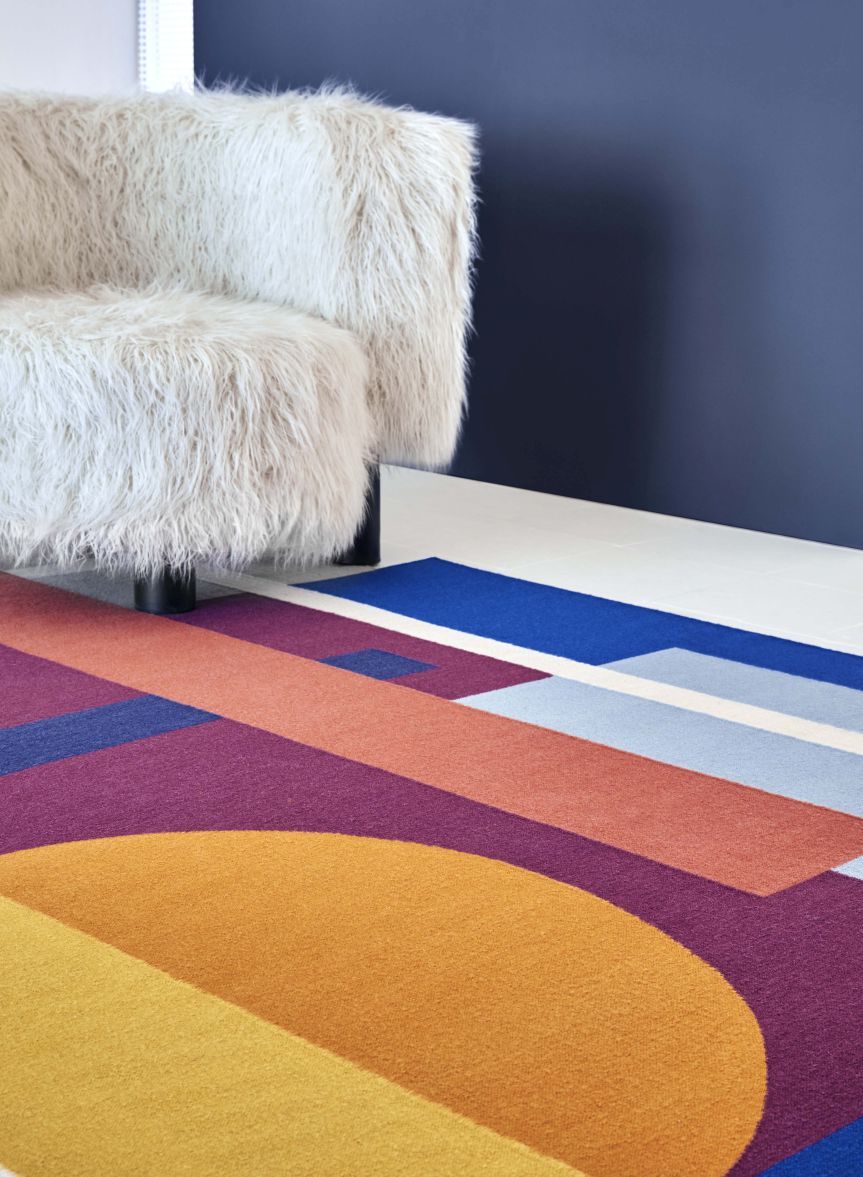 Detailansicht des Zoe Sool Teppichs von Gan mit geometrischen Formen und farbenfrohem Design neben einem Sessel.