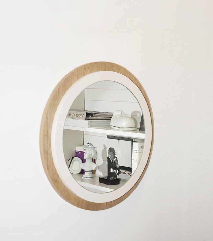 Runder Back to Bauhaus Spiegel mit Holzrahmen an weißer Wand, reflektiert Bücherregal.