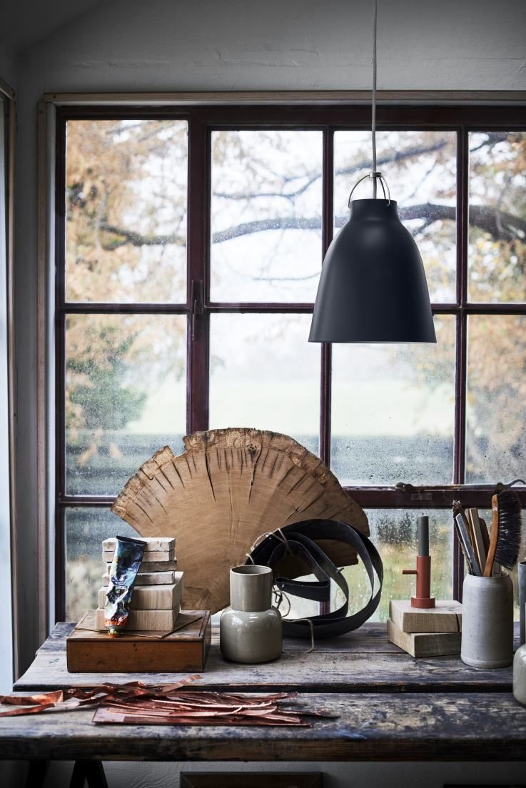 Schwarze Caravaggio Pendelleuchte von Fritz Hansen über einem Tisch mit künstlerischen Objekten vor Fenster.