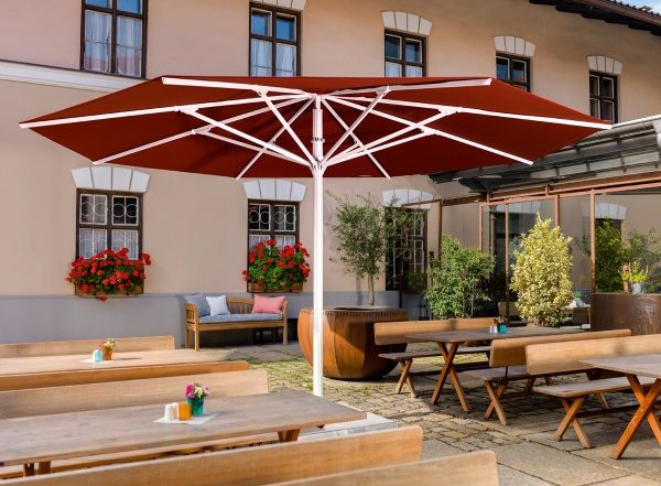 Weishäupl Sonnenschirm, ein großer, brauner Teleskopschirm spendet Schatten über Tischen und Bänken im Außenbereich.