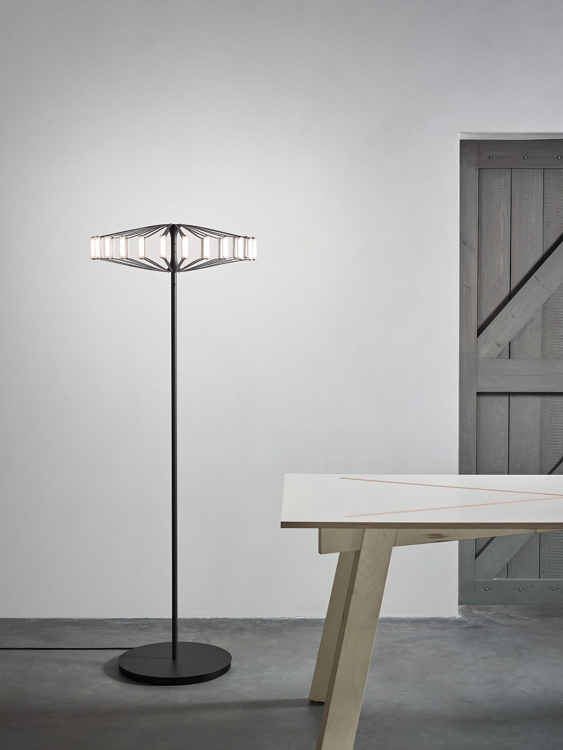 Moderne Wheel Floor Stehleuchte Japth in Schwarz mit geometrischem Lampenschirm und warmweißem Licht, neben Holztisch.