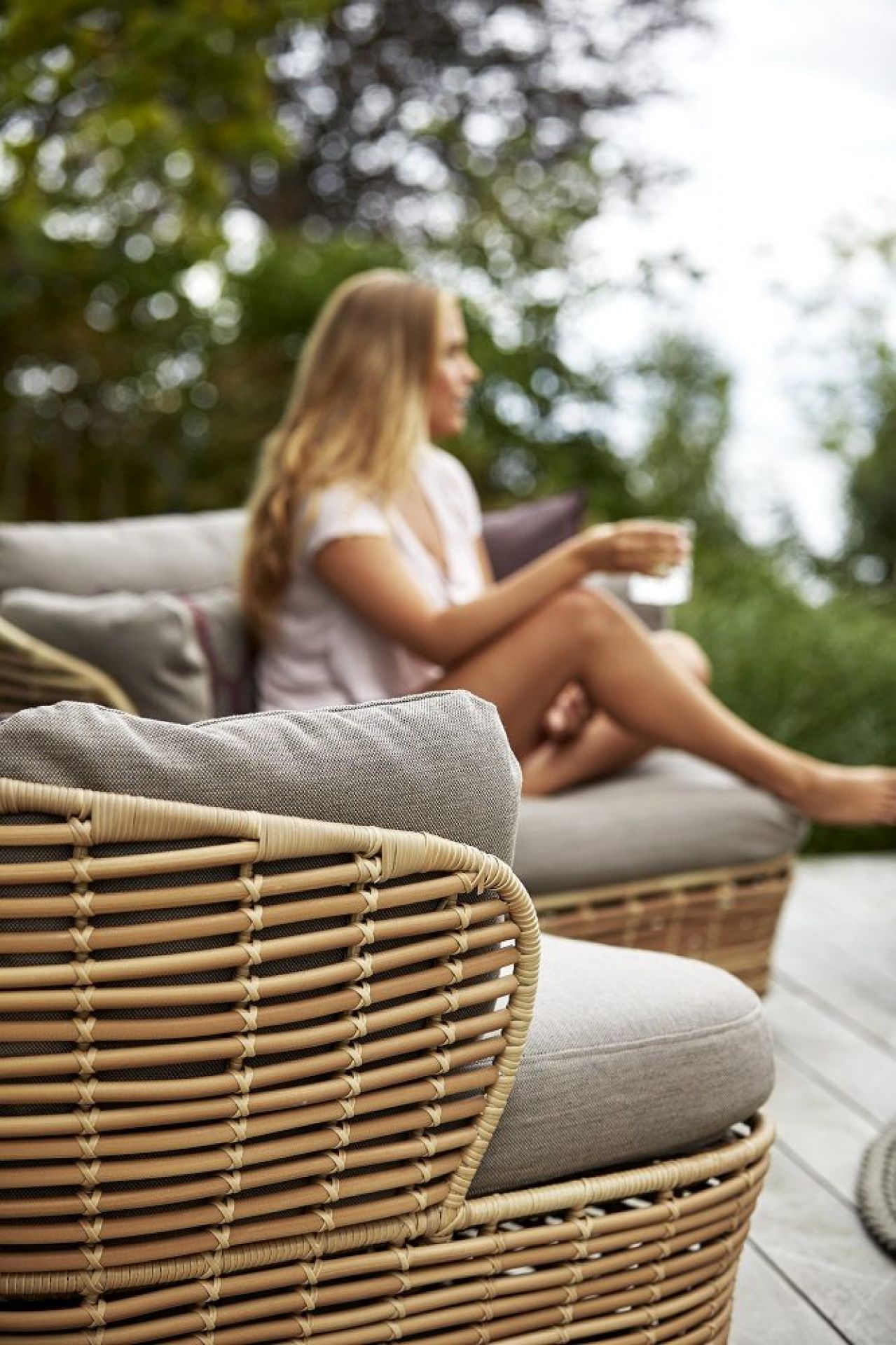 Nahaufnahme des Cane-Line Basket Outdoor Loungesessels aus Rattan mit grauen Kissen.
