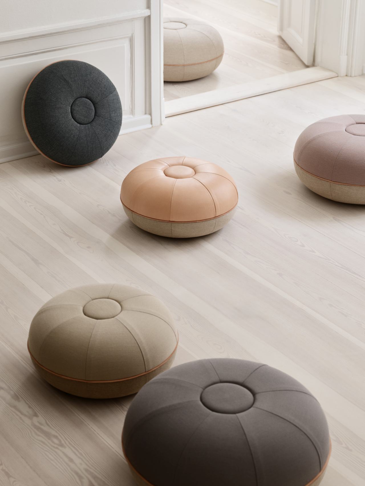 Mehrere Fritz Hansen Pouf Small Hocker in verschiedenen Farben auf hellem Holzboden.