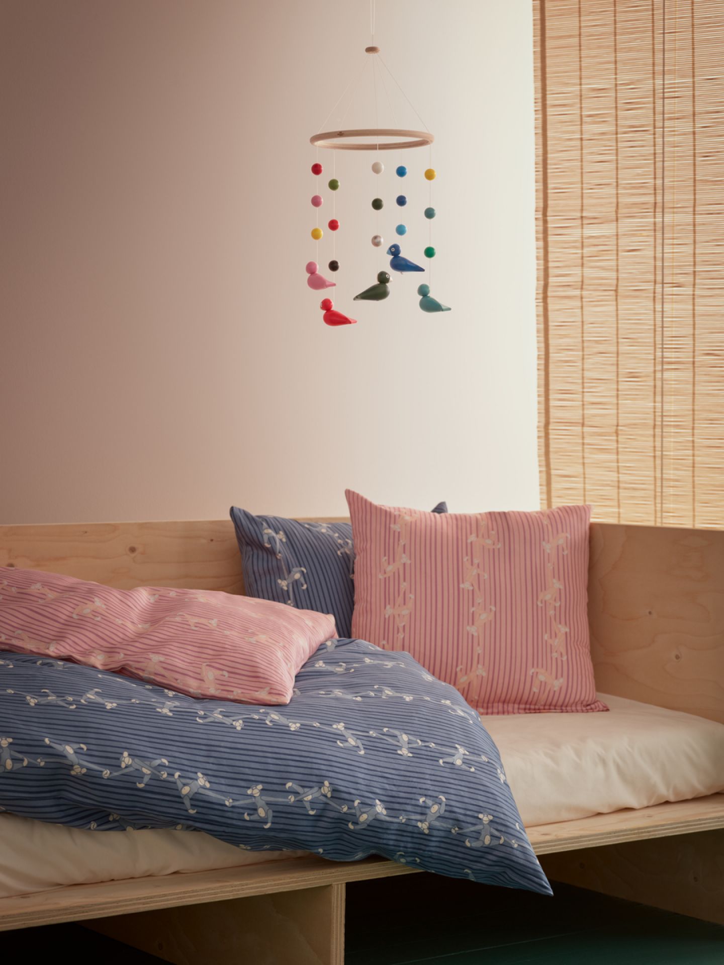 Uro Mobile Kay Bojesen über Kinderbett mit farbenfrohen Holzfiguren und Kugeln, skandinavisches Design.