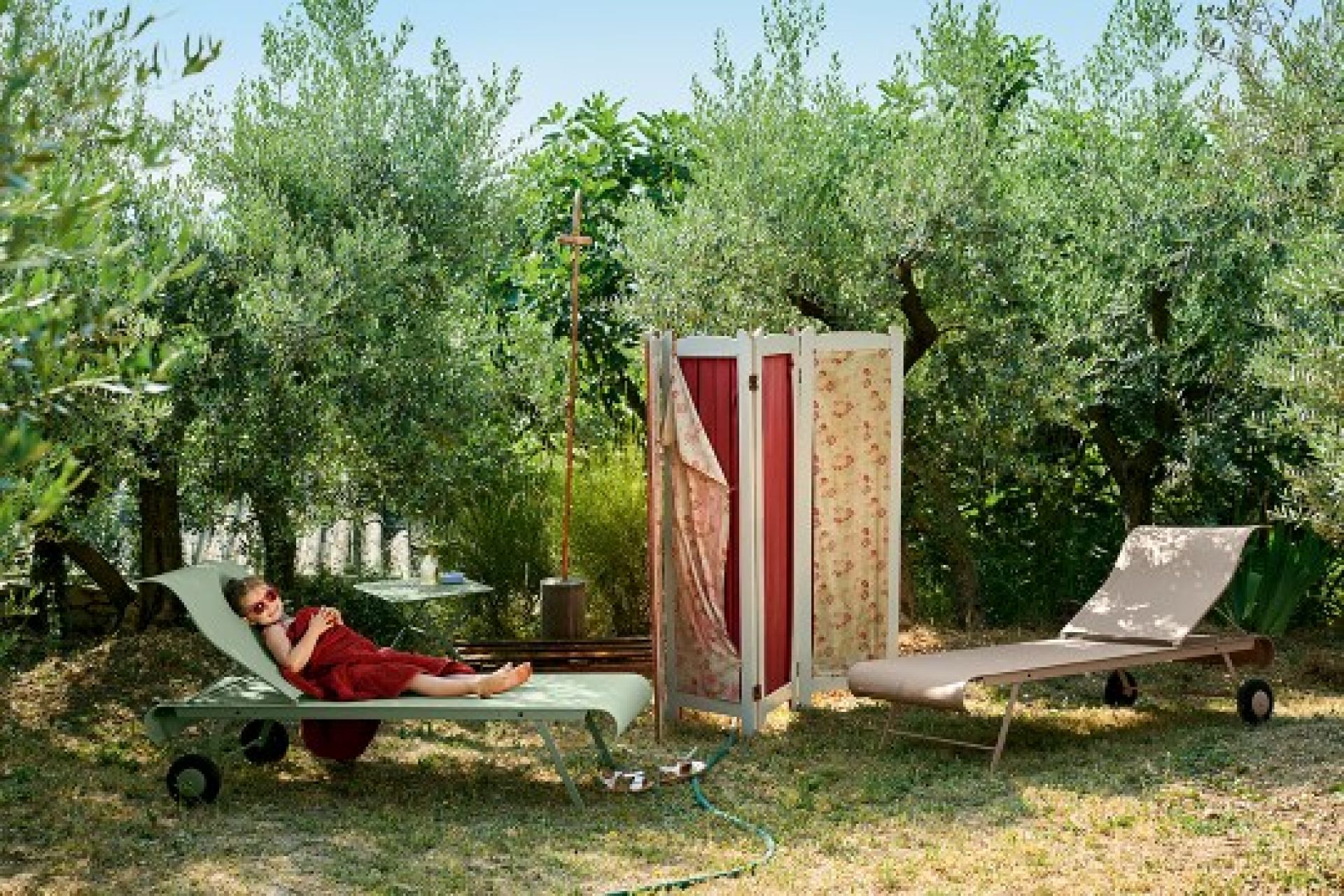 Dune Sonnenliege von Fermob im Garten: Mädchen entspannt auf der Liege mit Rädern.