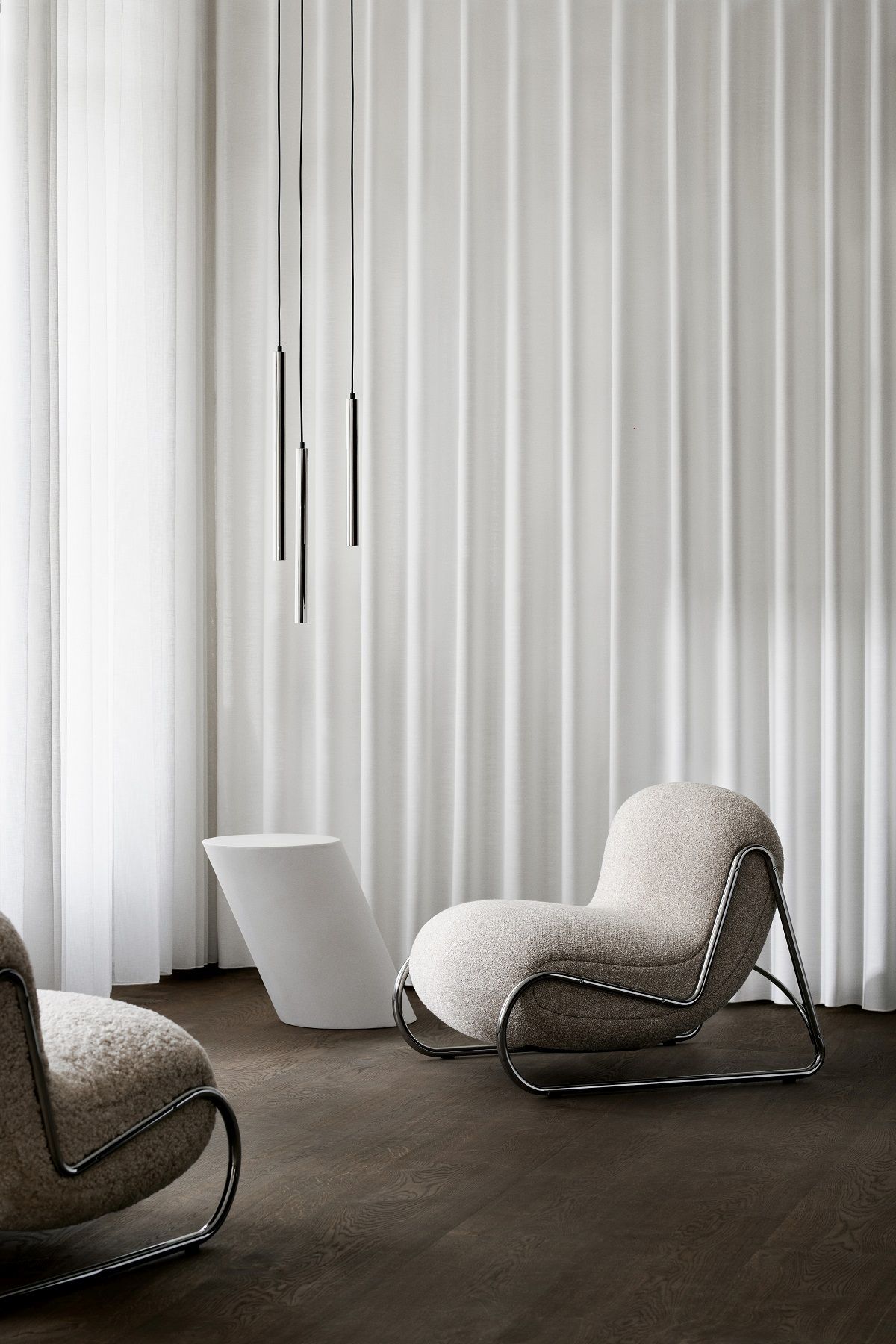 Beiger NORR11 Boho Armchair Sessel mit Chromgestell vor weißem Vorhang und dunklem Holzboden.