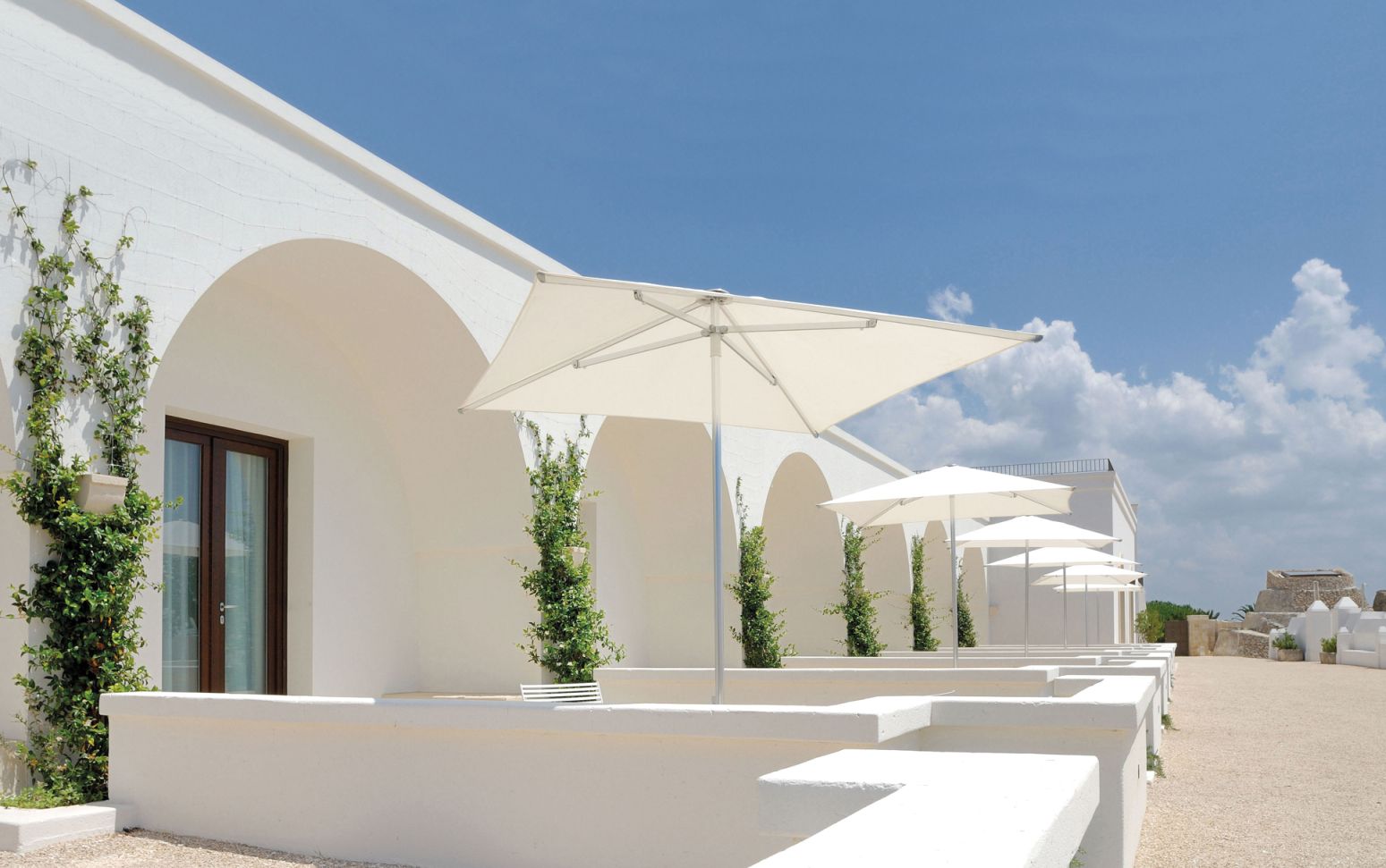 Reihe weißer Shade Sonnenschirme von Emu im Außenbereich vor weißer Architektur.