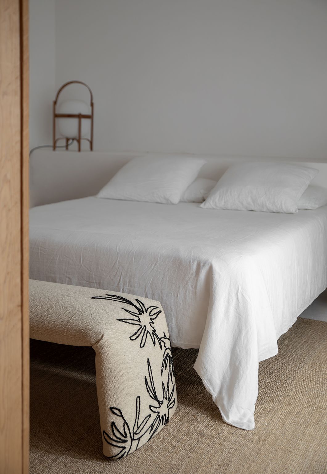 Beige Bank mit Blumenmuster vor weißem Bett, Nanimarquina Bankhocker für Schlafzimmer.