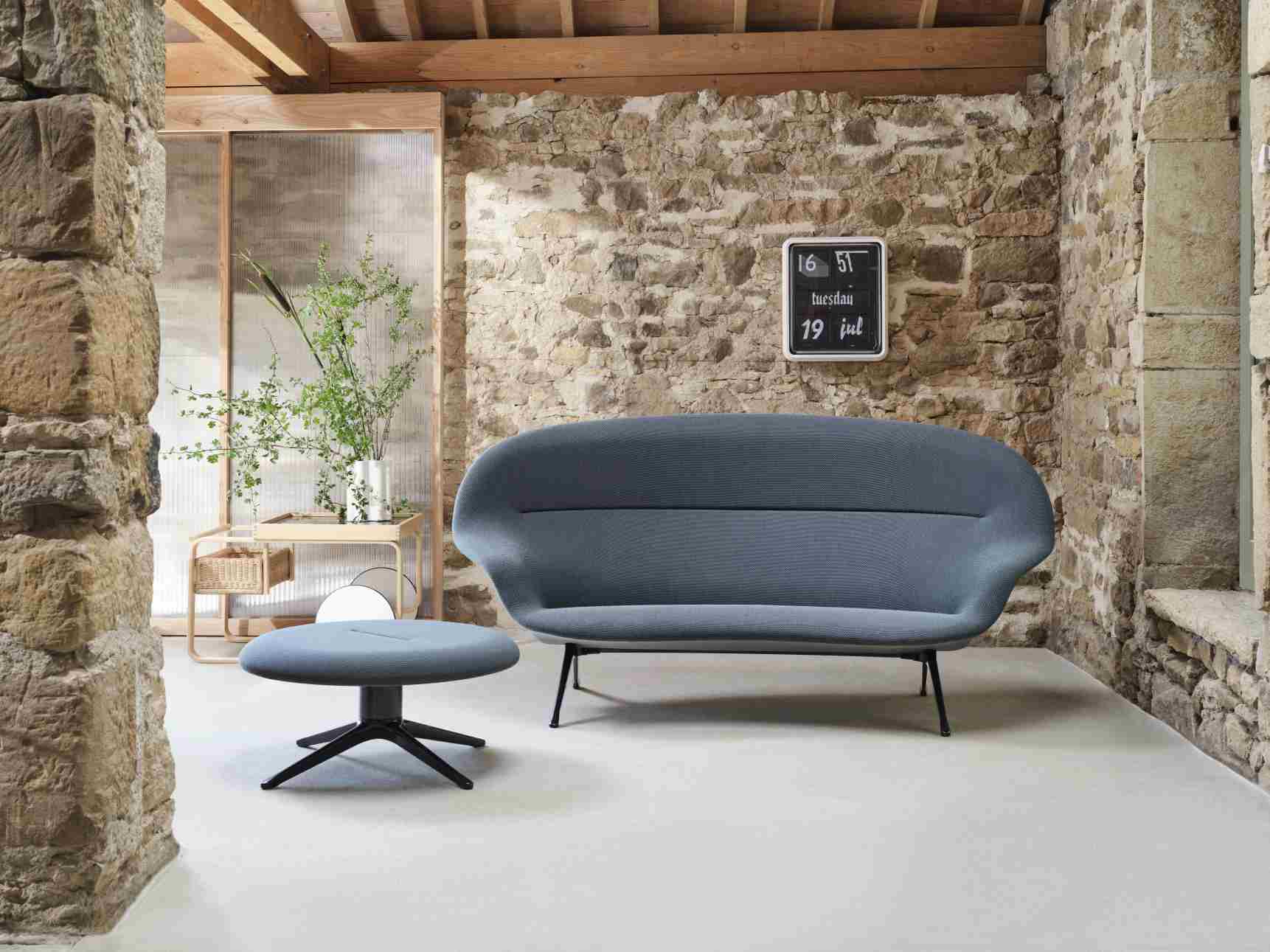 Abalon Sofa von Vitra in blau mit passendem Hocker vor einer Steinwand.