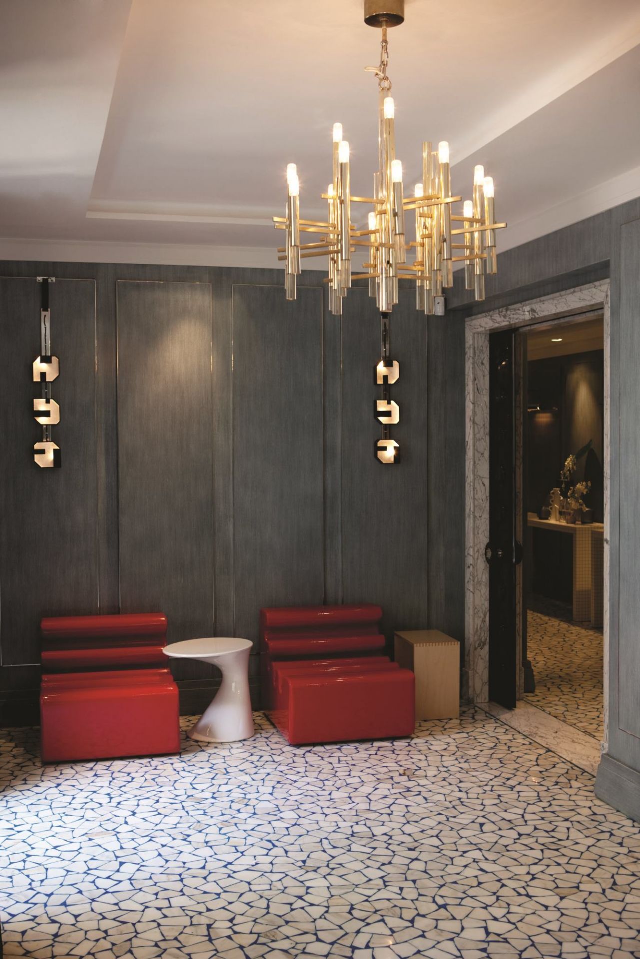 Elegantes Interieur mit roter Sitzgruppe und weißem Zanotta Tod Couchtisch unter einem goldenen Kronleuchter.