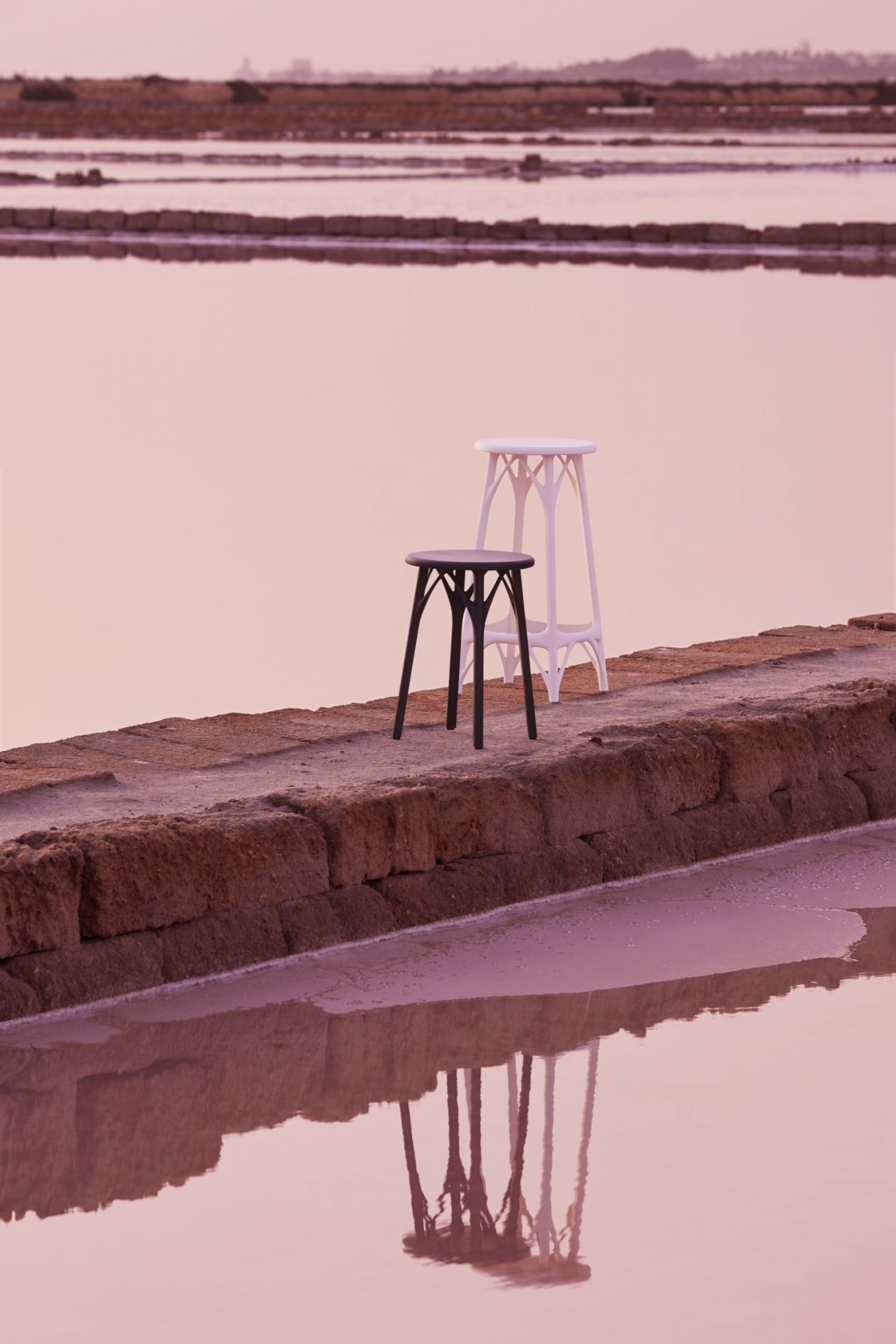 Schwarzer A.I. Hocker von Kartell, Höhe 45cm, auf Steinmauer vor rosa Hintergrund. Design Hocker.