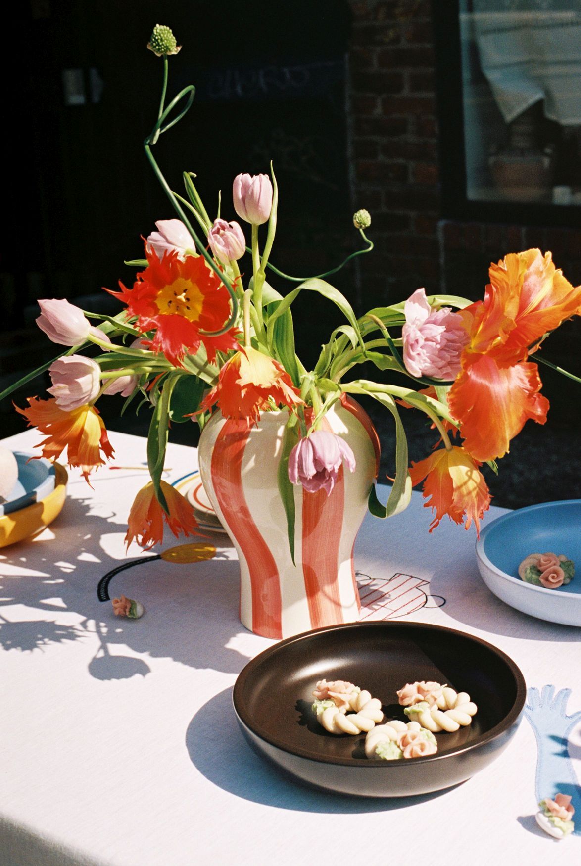 Rote Strip Vase von Hay, gefüllt mit bunten Tulpen, auf einem gedeckten Tisch.