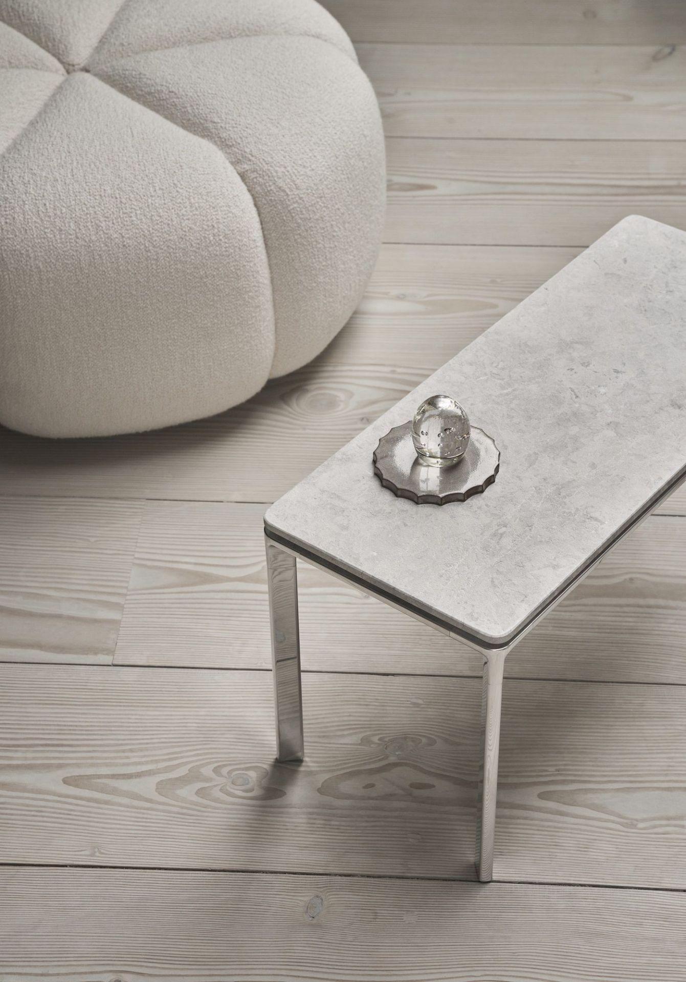 Rechteckiger Vipp Couchtisch mit Marmorplatte und Deko-Objekt, neben einem runden, weißen Sitzhocker.