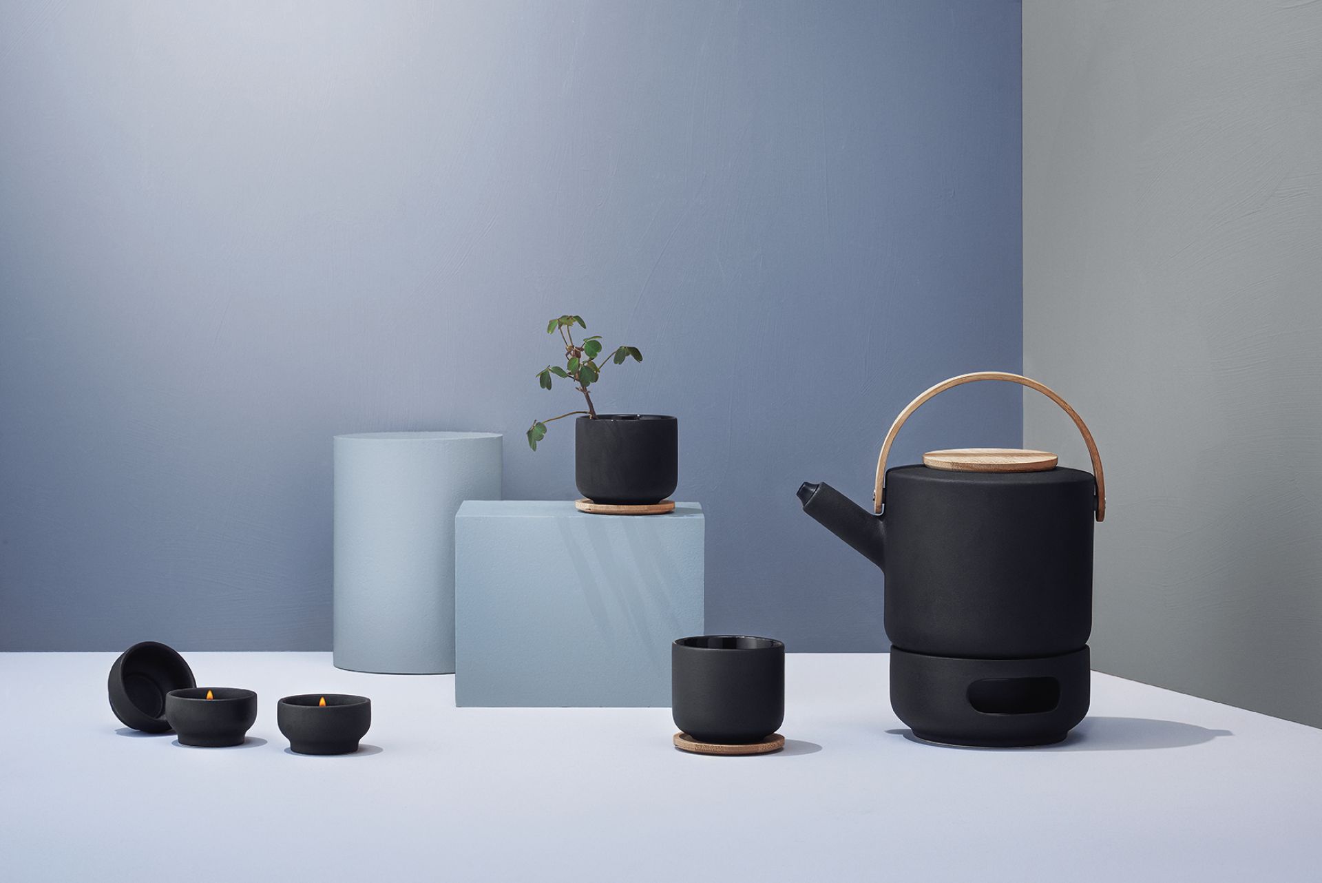 Produktfoto: Schwarzes Stelton Theo Stövchen mit Teelichtern, Teekanne und Tasse für gemütliche Teezubereitung.