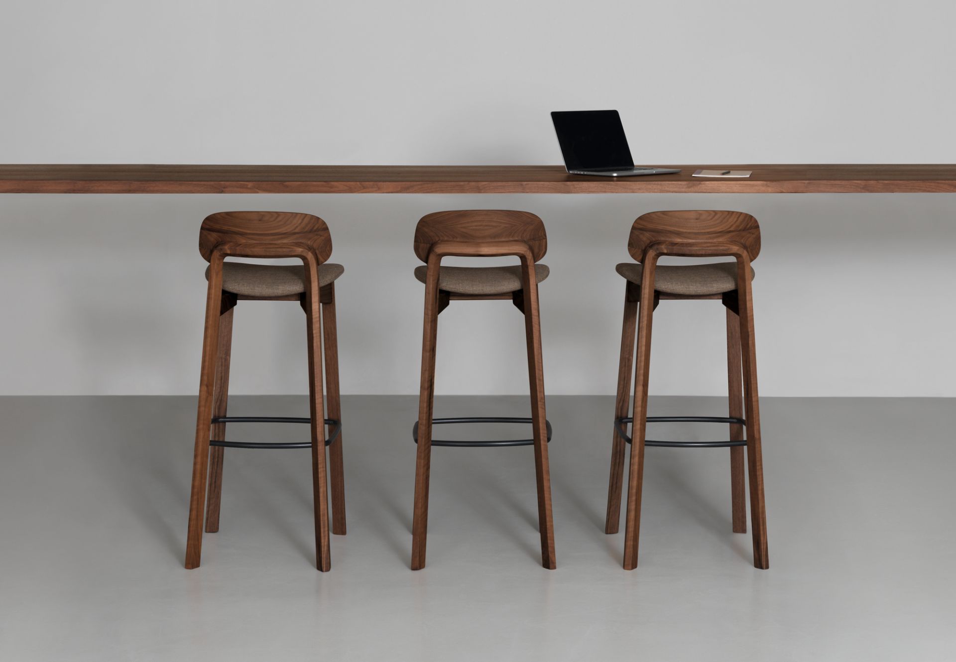 Drei Nonoto Barhocker aus Nussbaumholz mit 80cm Sitzhöhe vor einer Theke.