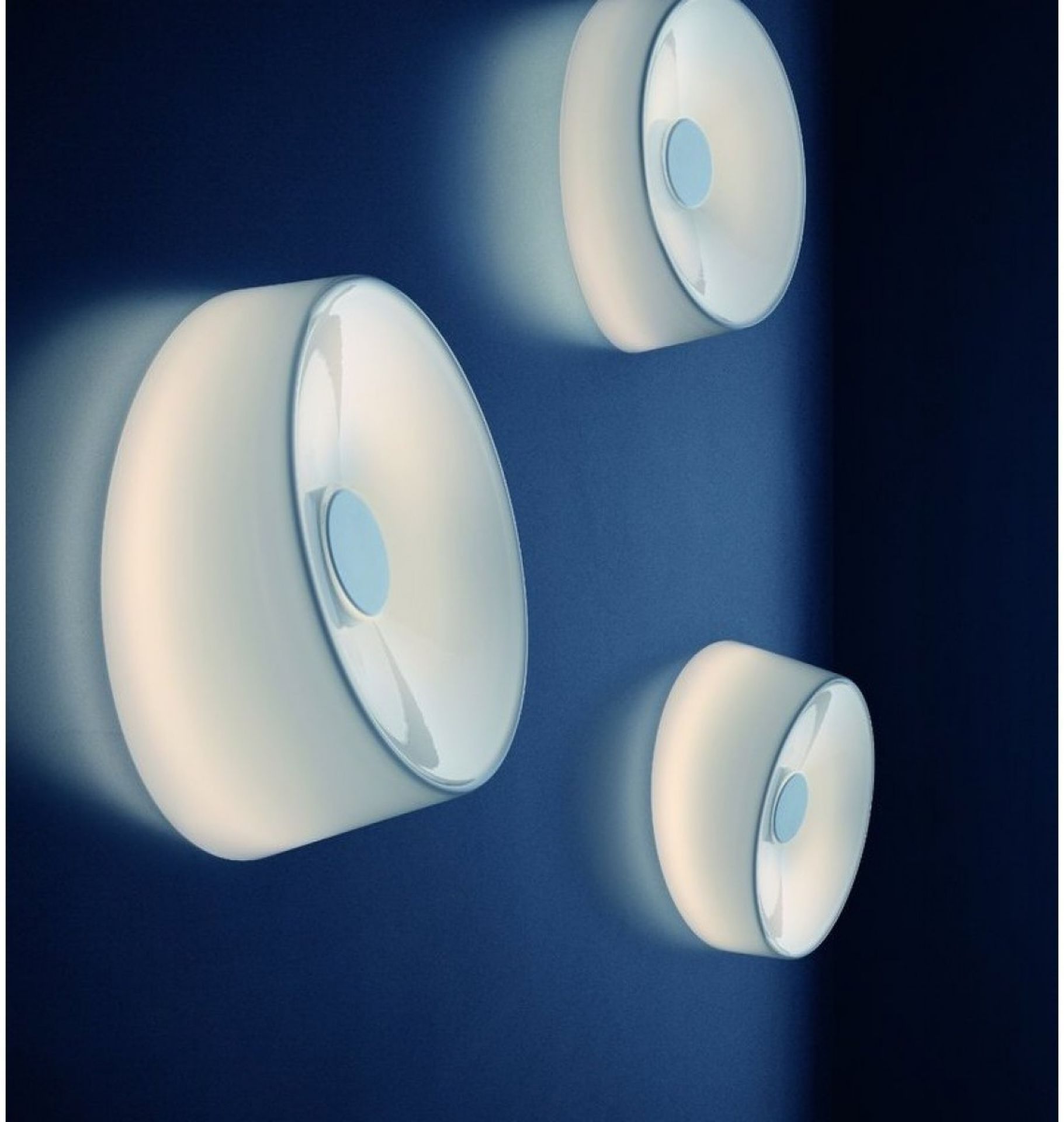 Drei graue Lumiere Wandleuchten / Deckenleuchten an einer blauen Wand. Moderne Innenbeleuchtung.