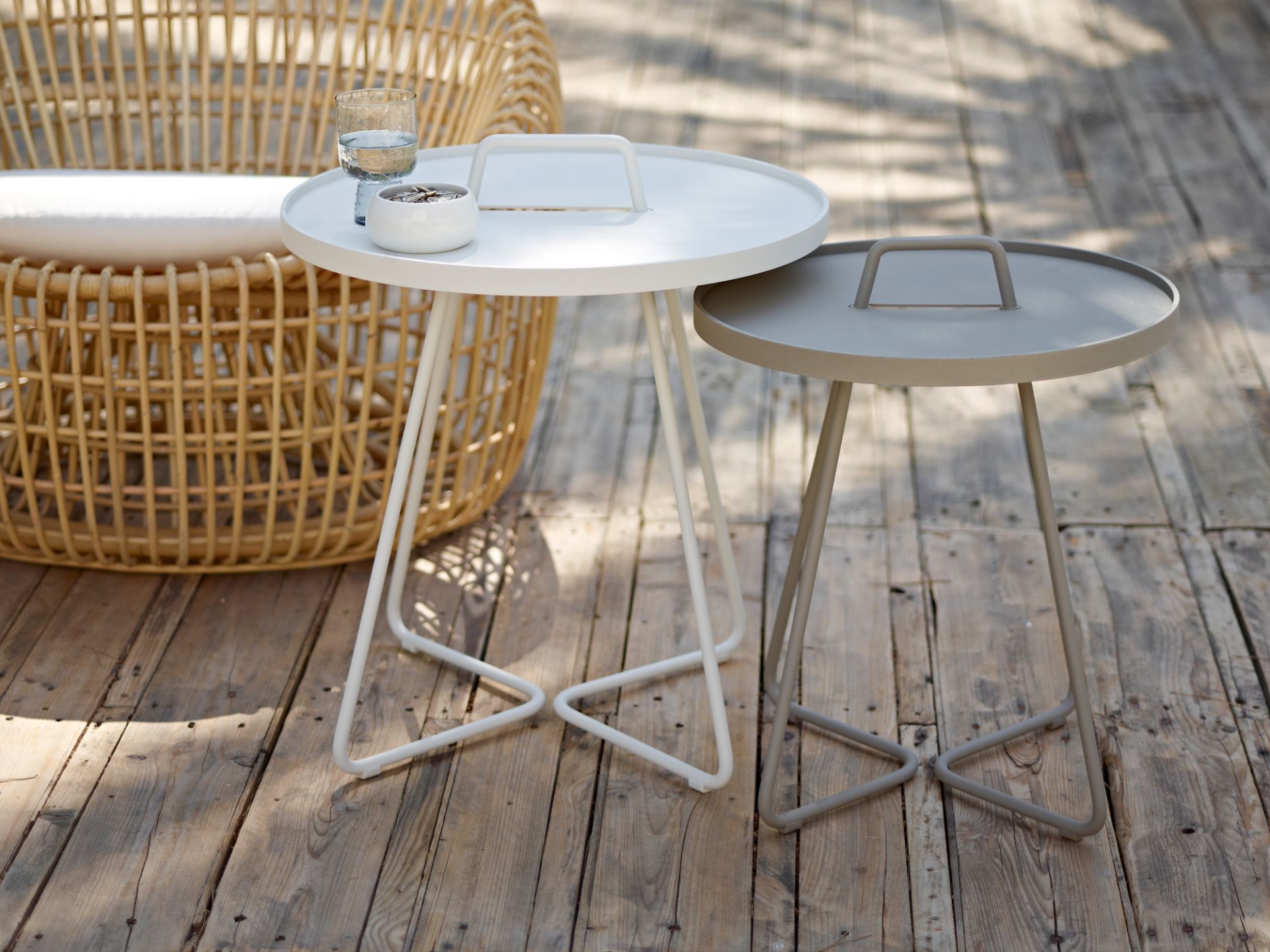 Zwei Cane-Line On-The-Move Beistelltische in Weiß und Grau auf einer Holzterrasse.