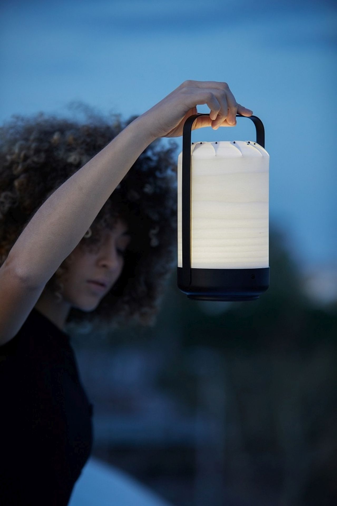 Frau hält Chou Mini LED Akkuleuchte von LZF Lamps hoch. Tischleuchte mit USB.