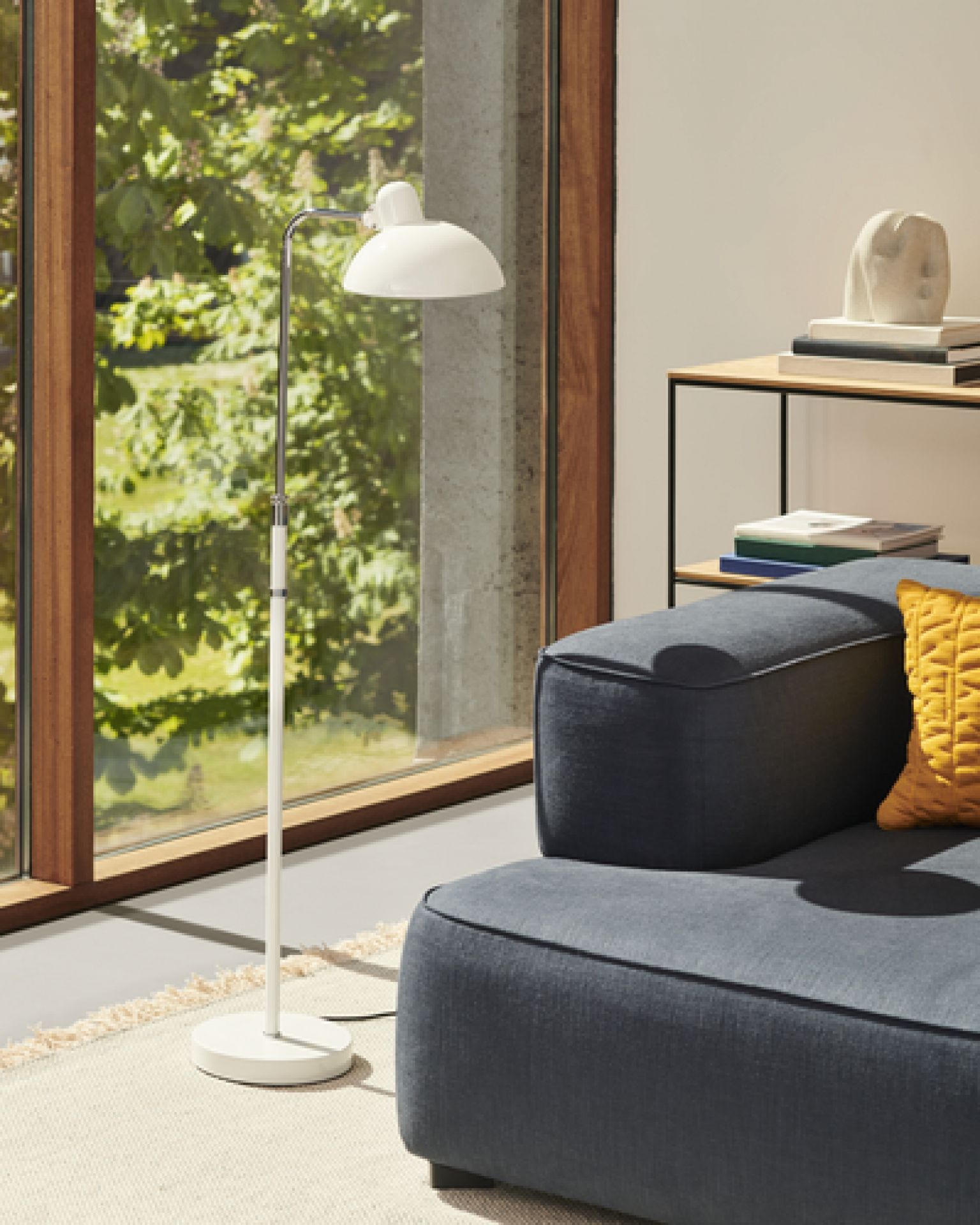 Wohnzimmer mit Fritz Hansen Regal, Stehlampe und blauem Sofa. Modernes Wohnen.