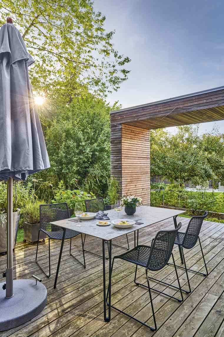 Weishäupl Trend Schirm spendet Schatten über Esstisch mit vier Stühlen im Garten.