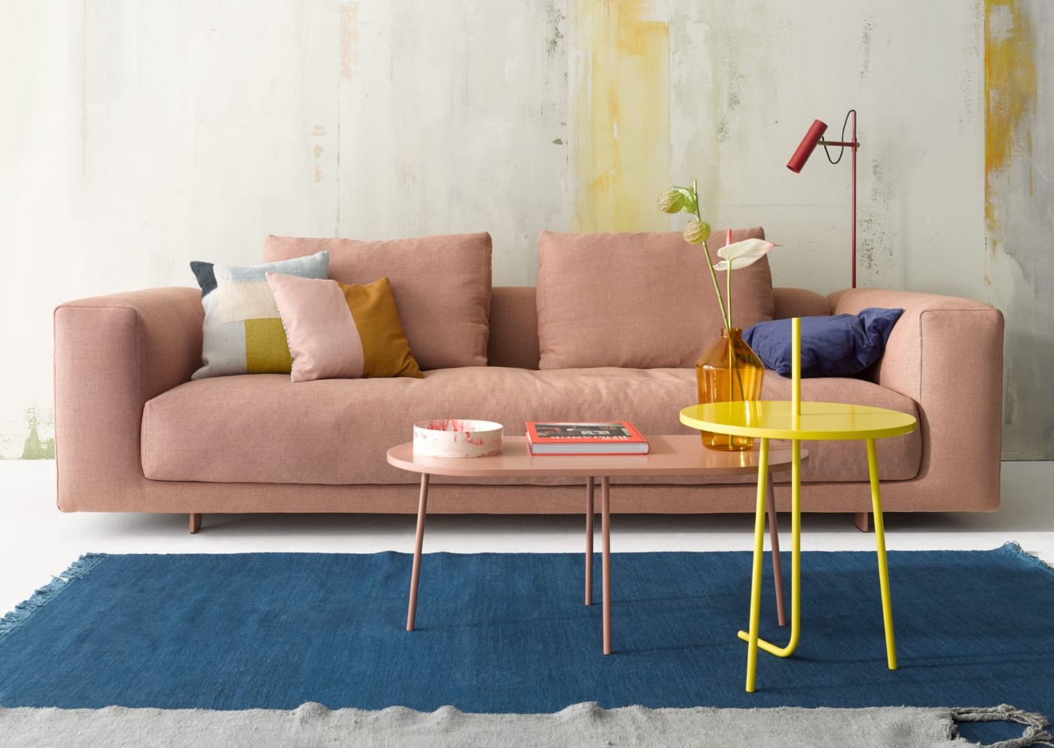 Ovaler Bond Couchtisch in Rosa vor Sofa und blauem Teppich. Moderner Wohnzimmertisch.
