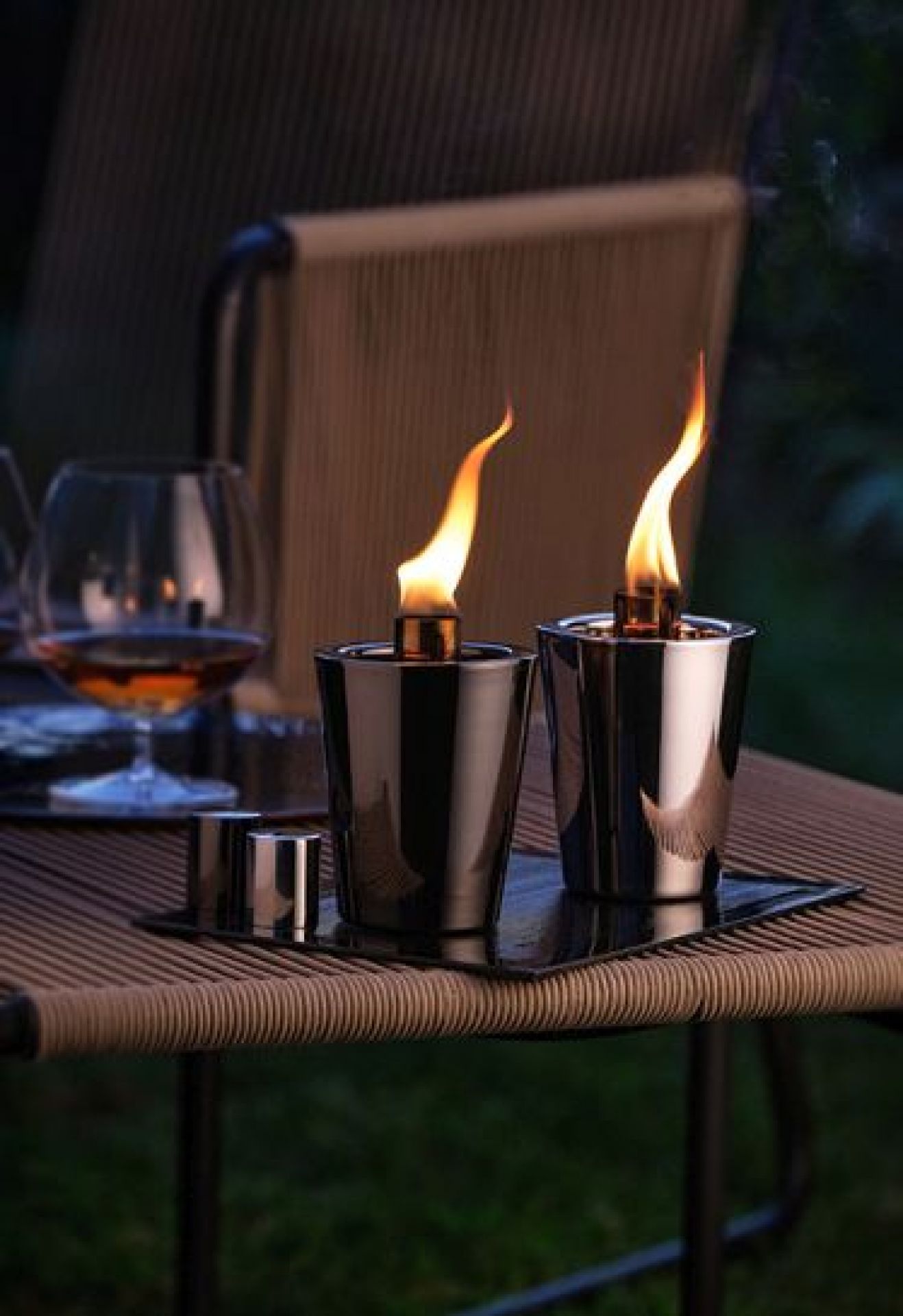 Zwei brennende, schwarze Tarcia Tischfackeln von Philippi auf einem Tisch im Freien, stimmungsvolle Gartenbeleuchtung.