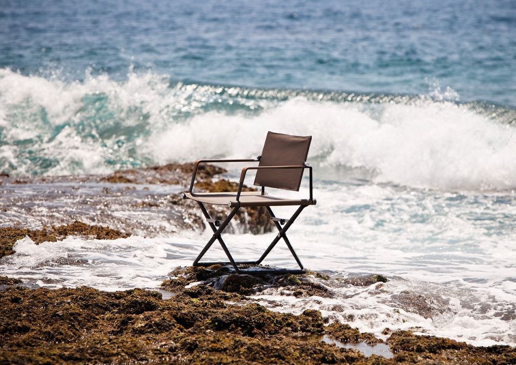 SeaX Armchair von Dedon am Strand, brauner Outdoor Armlehnstuhl mit Meer im Hintergrund.