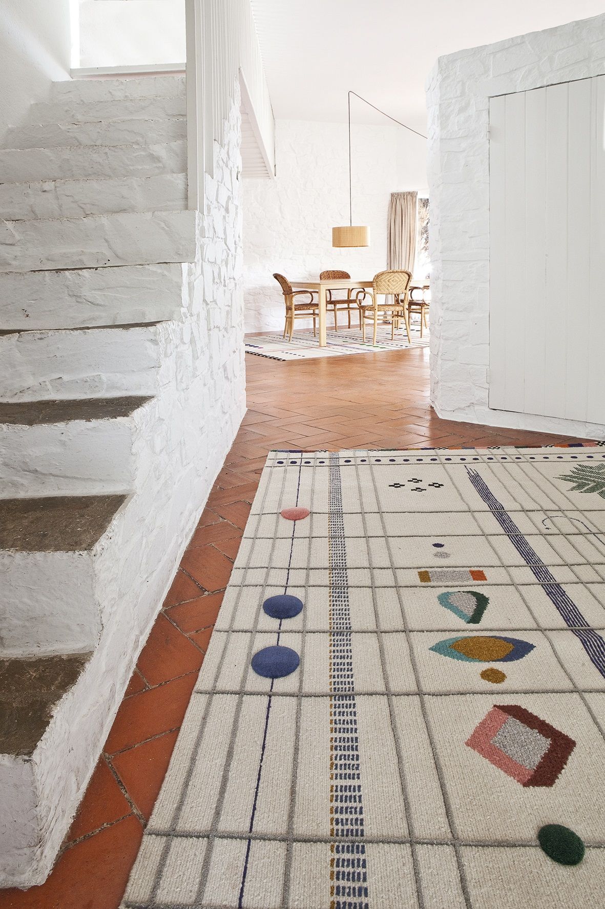 Rabari Teppich von Nanimarquina in hellem Raum mit Treppe und Essbereich. Moderner Wollteppich mit geometrischen Mustern.