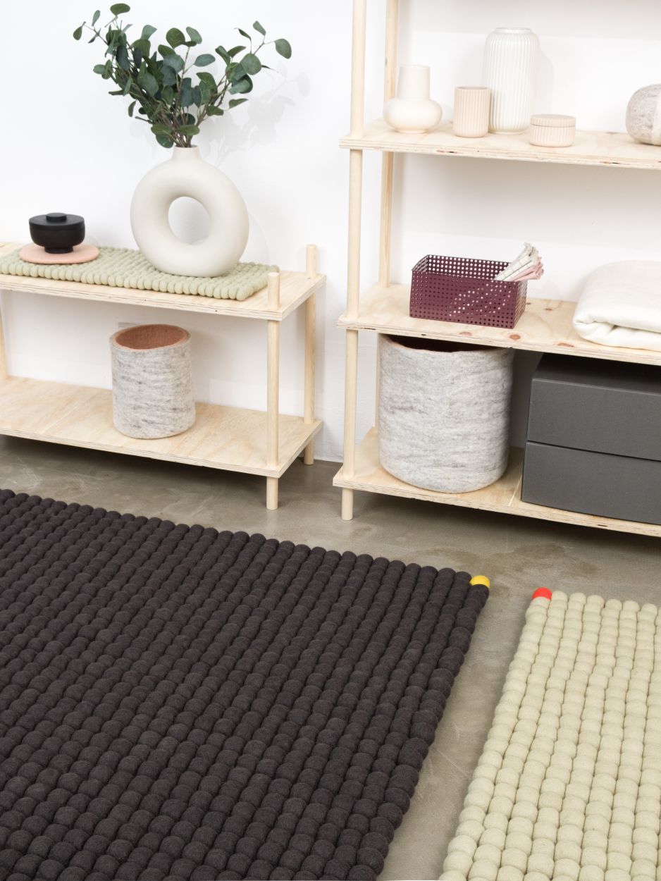 Anthrazitfarbener Filzteppich "Big One" von myfelt (180x260 cm) im Interieur mit Regalen. Rechteckiger Wollfilzteppich.