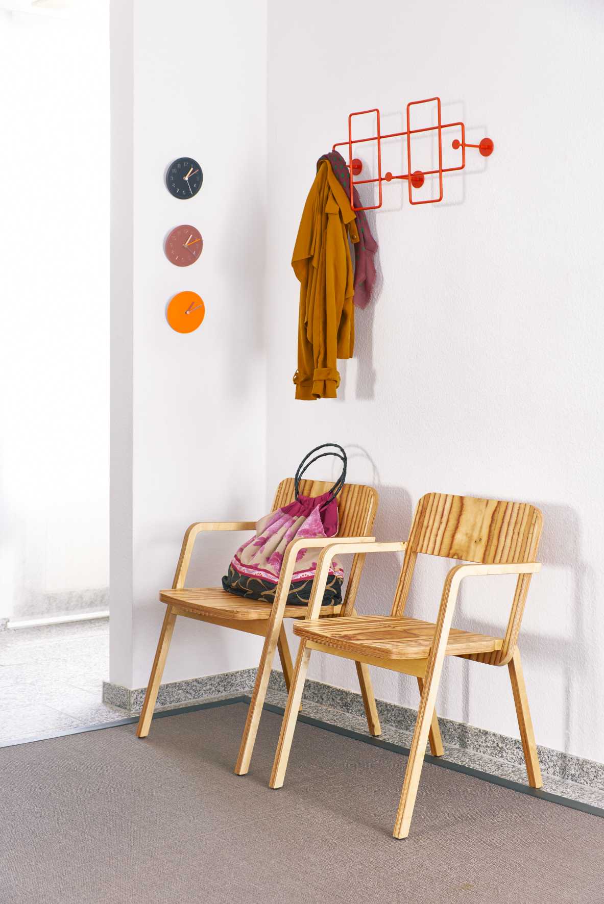 Flur mit Richard Lampert Bazar Wandgarderobe in Rot, Jacken und zwei Holzstühlen.