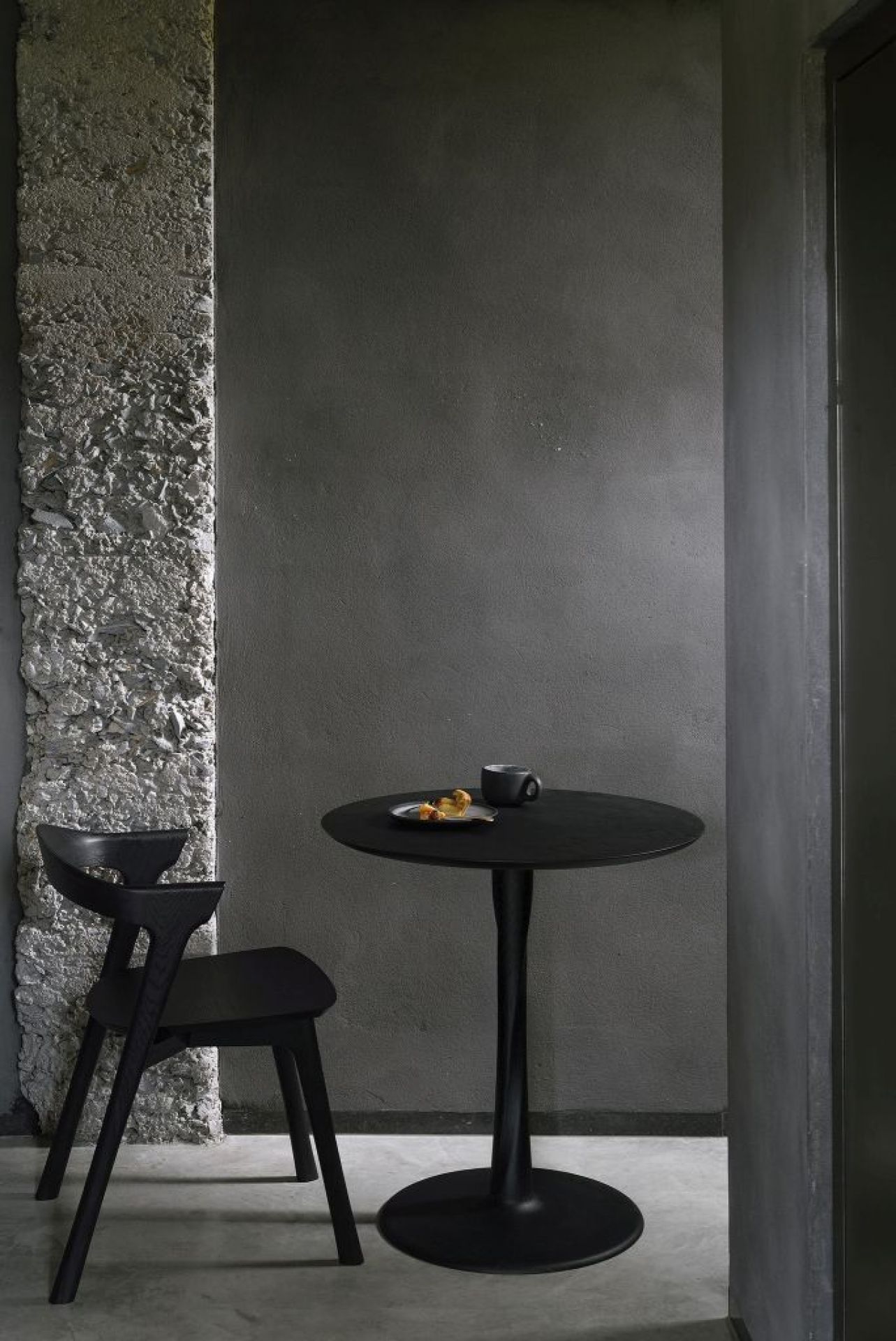 Schwarzer Ethnicraft Torsion Eiche Tisch mit Stuhl und Speisen in minimalistischem Interieur.