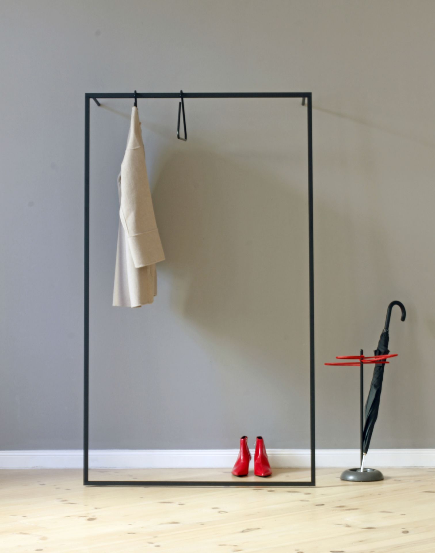 Roomsafari Leano Anlehngarderobe mit Mantel, roten Schuhen und Schirmständer vor grauer Wand. Moderne Garderobenlösung.